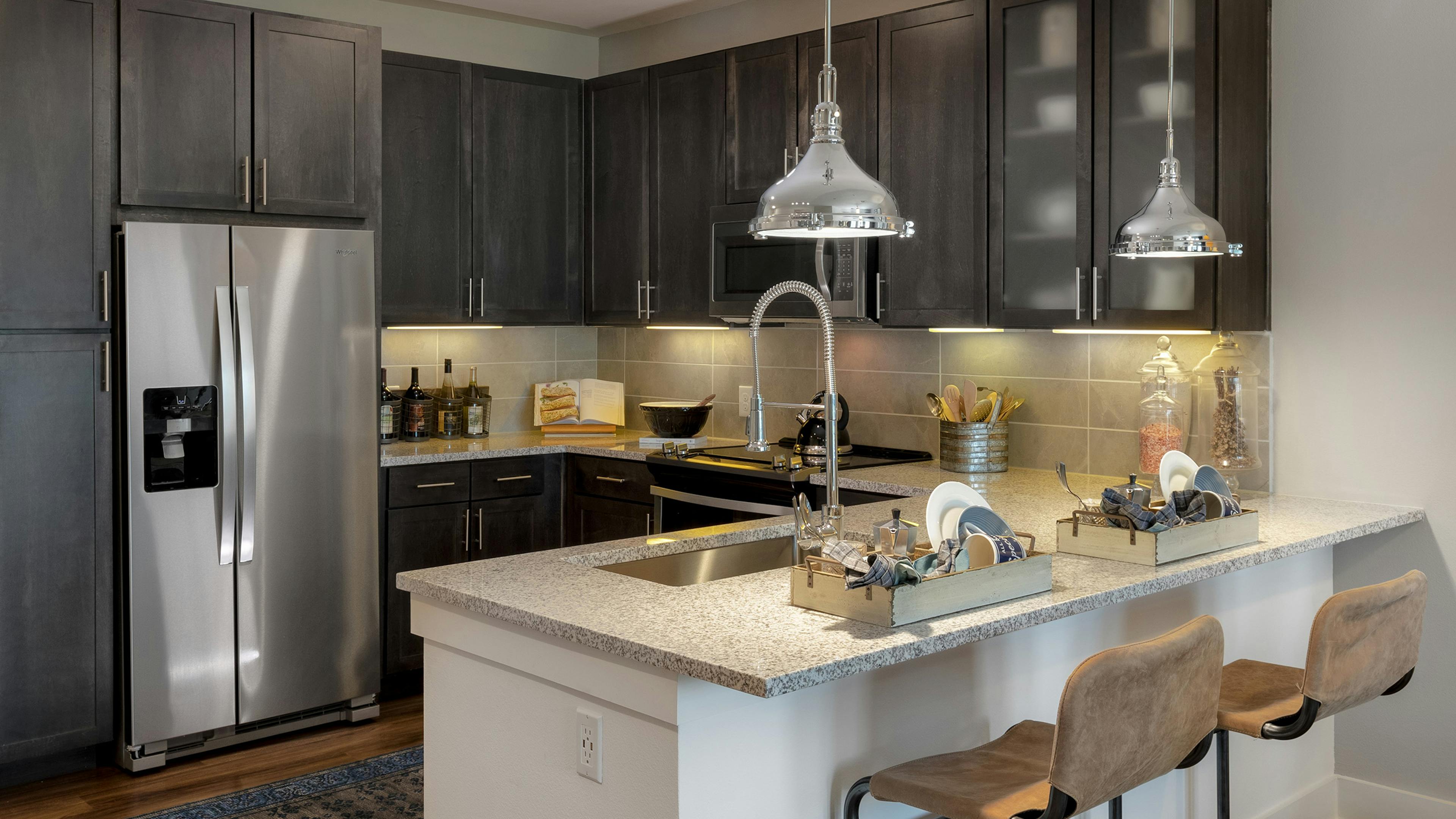 AMLI Grapevine apartment kitchen with granite countertops and stainless steel appliances and 2 silver hanging pendant lights