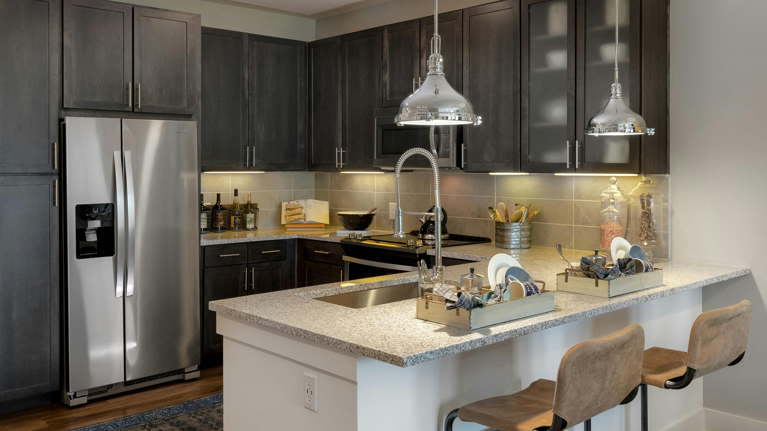 AMLI Grapevine apartment kitchen with granite countertops and stainless steel appliances and 2 silver hanging pendant lights