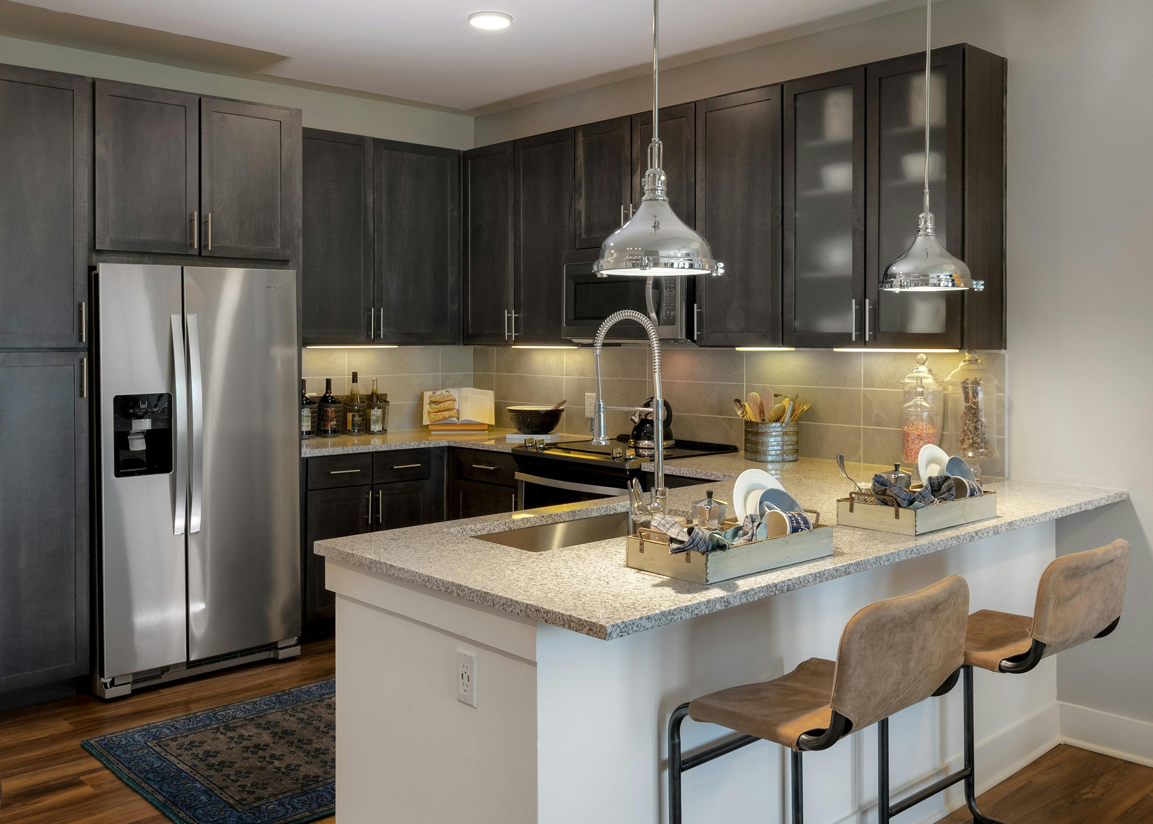 AMLI Grapevine apartment kitchen with granite countertops and stainless steel appliances and 2 silver hanging pendant lights