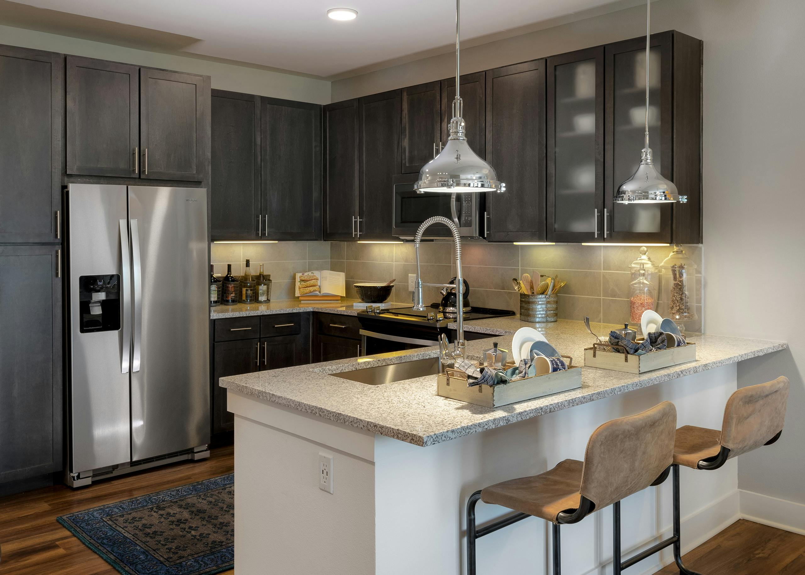 AMLI Grapevine apartment kitchen with granite countertops and stainless steel appliances and 2 silver hanging pendant lights