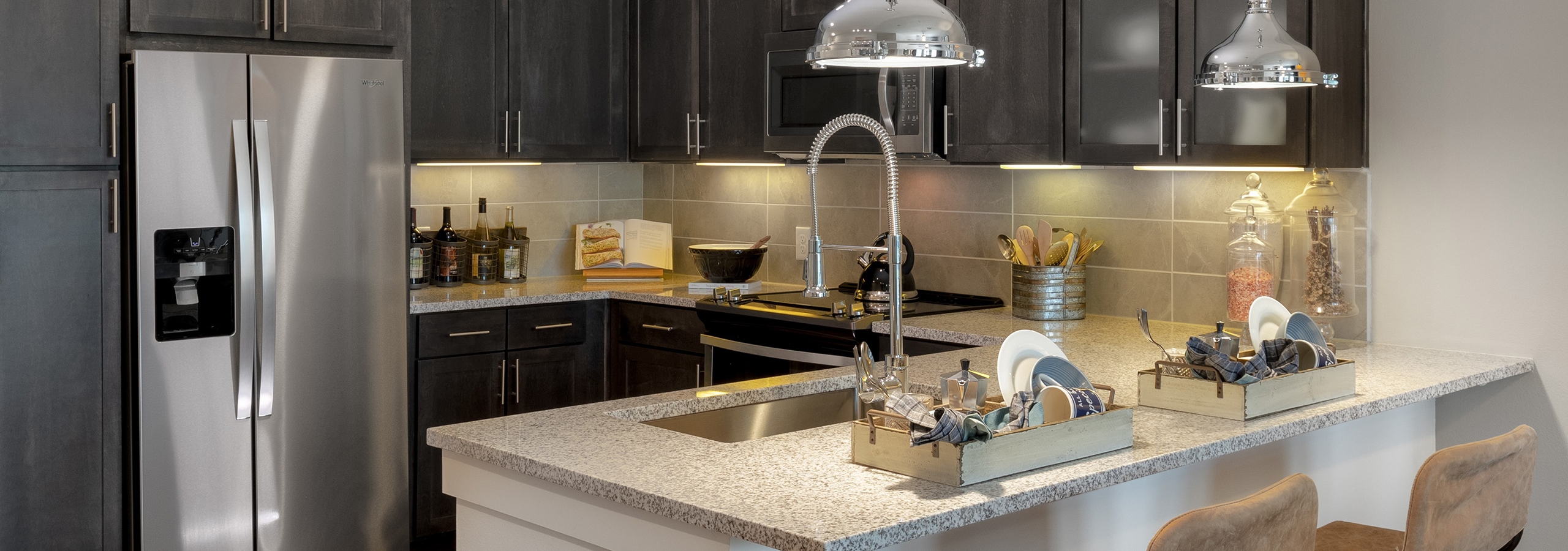 AMLI Grapevine apartment kitchen with granite countertops and stainless steel appliances and 2 silver hanging pendant lights