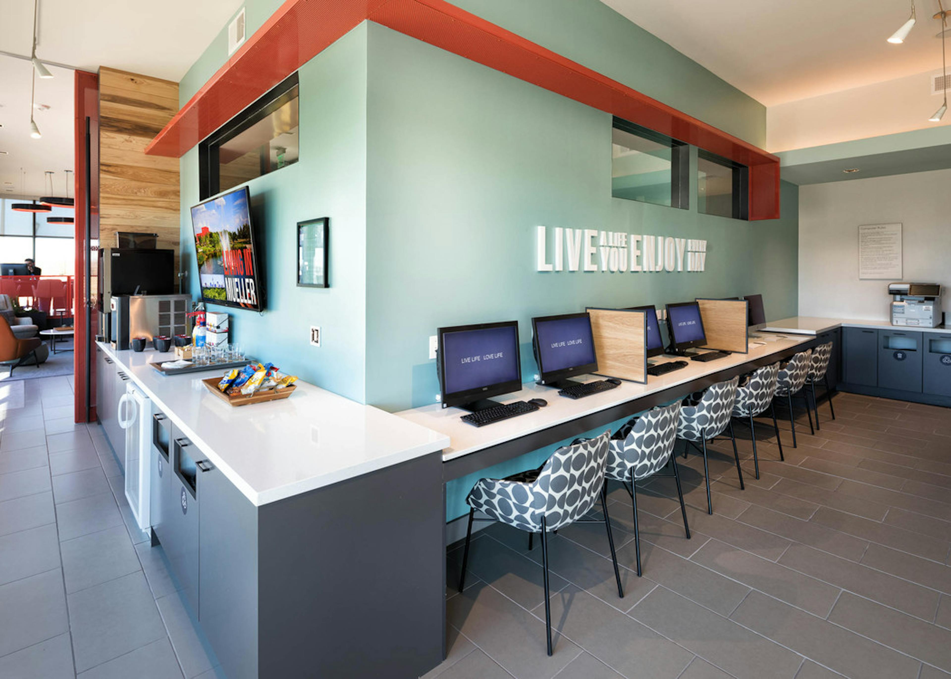 Tech lounge at AMLI on Aldrich with desktop computers at a long white desk against a light teal wall with patterned chairs