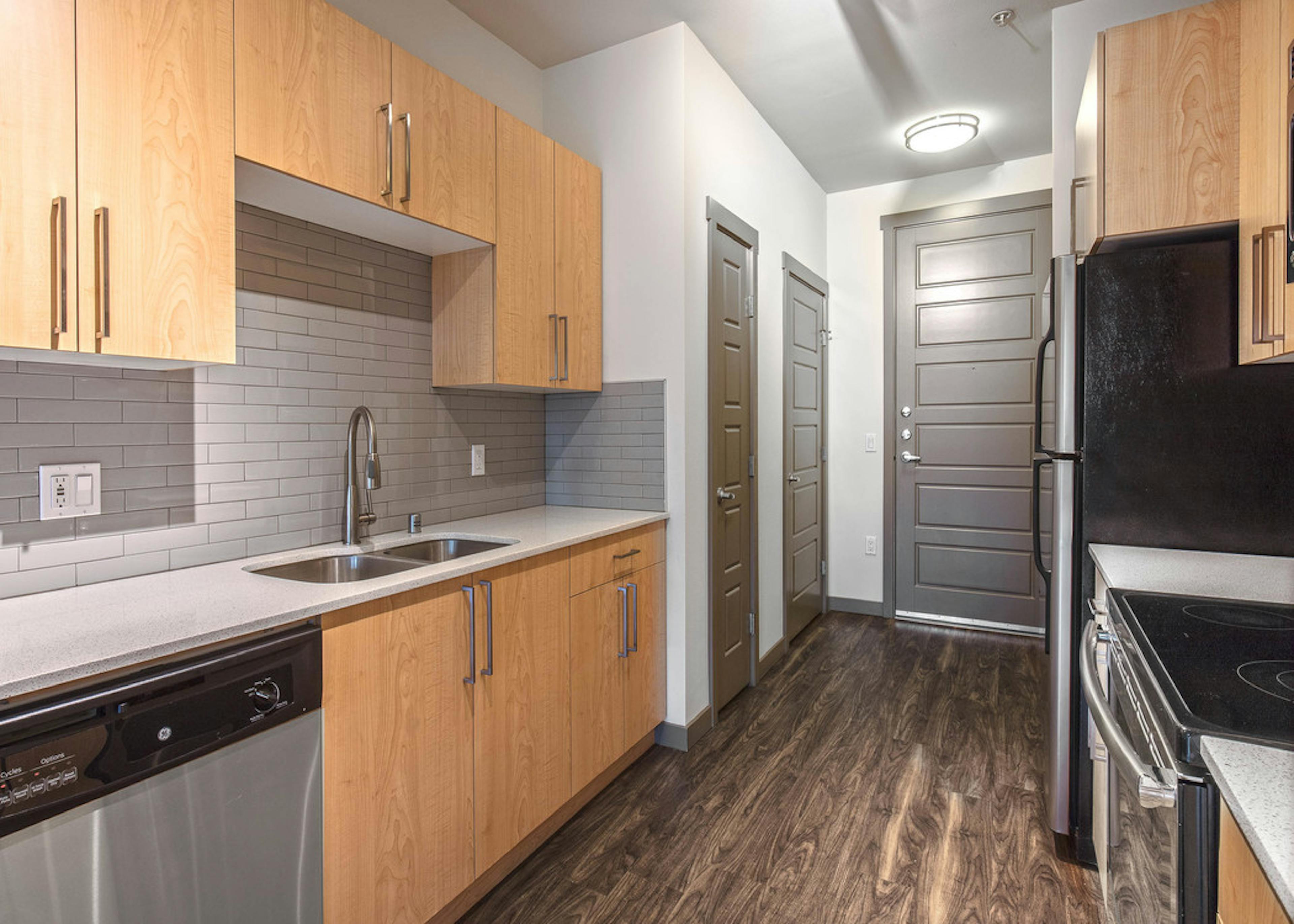 Interior view of AMLI Mark24 apartment kitchen with light cabinets white quartz counter tops and grey back splash  