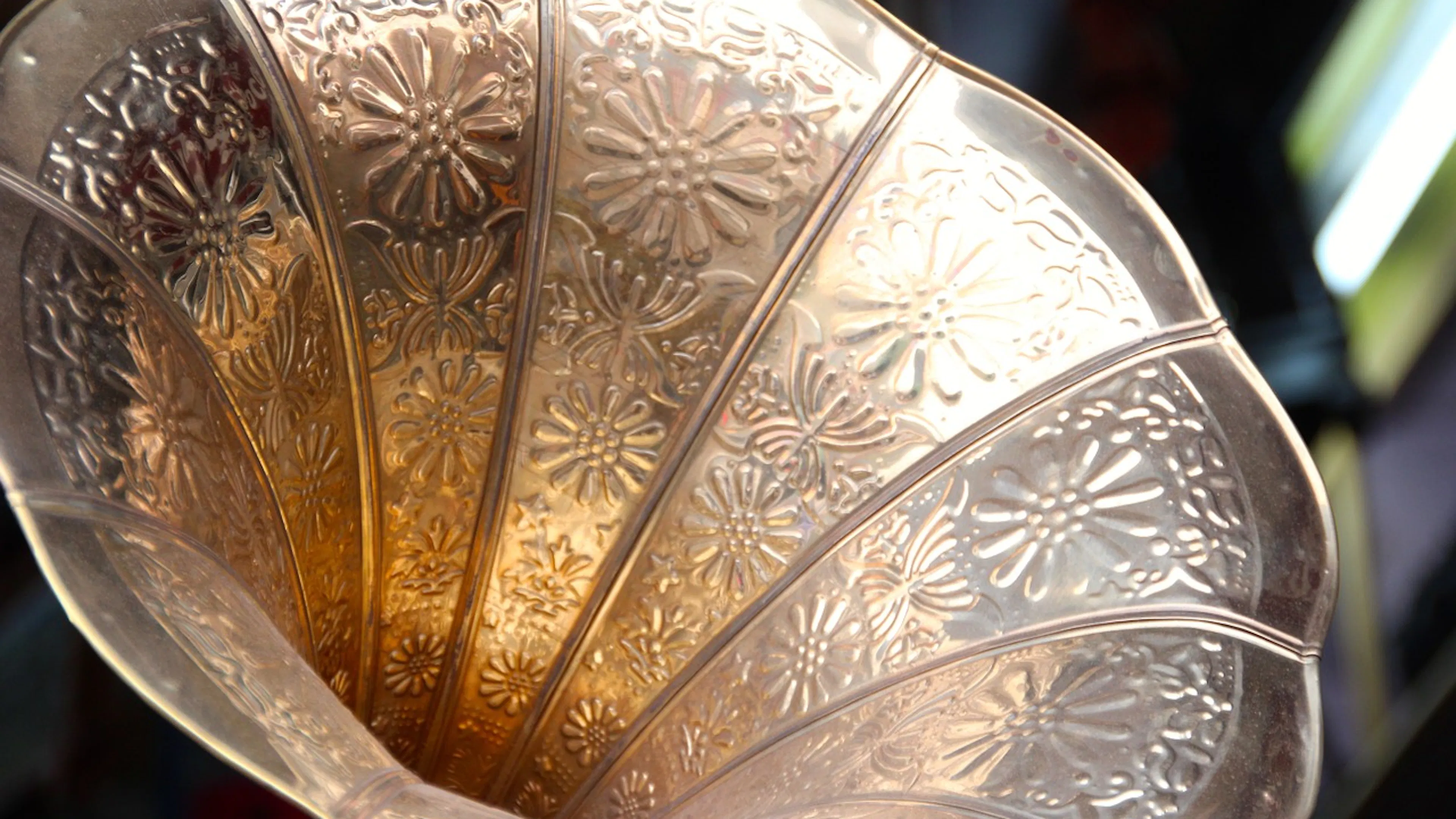 Close up of an antique brass gramophone horn with an intricate stamped floral design