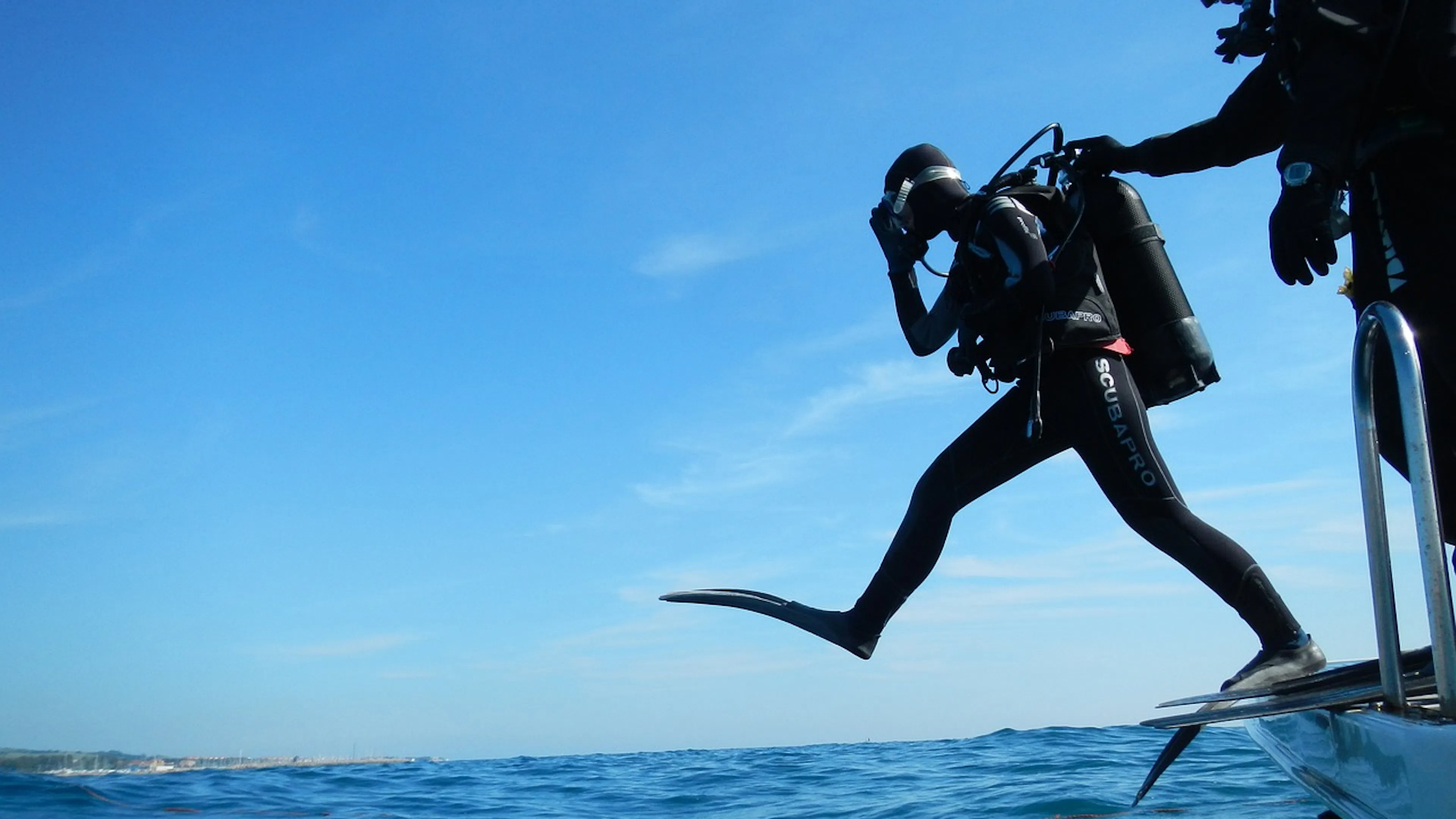 A scuba diver taking a big leap step off a boat into calm blue ocean waters on a sunny day