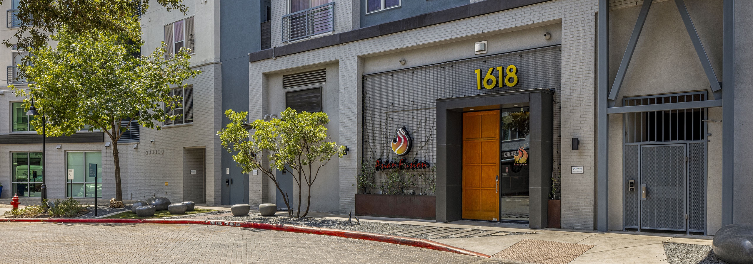 AMLI South Shore building with gray façade with large 1618 and Asian Fusion signage and brown wood door and bridge above