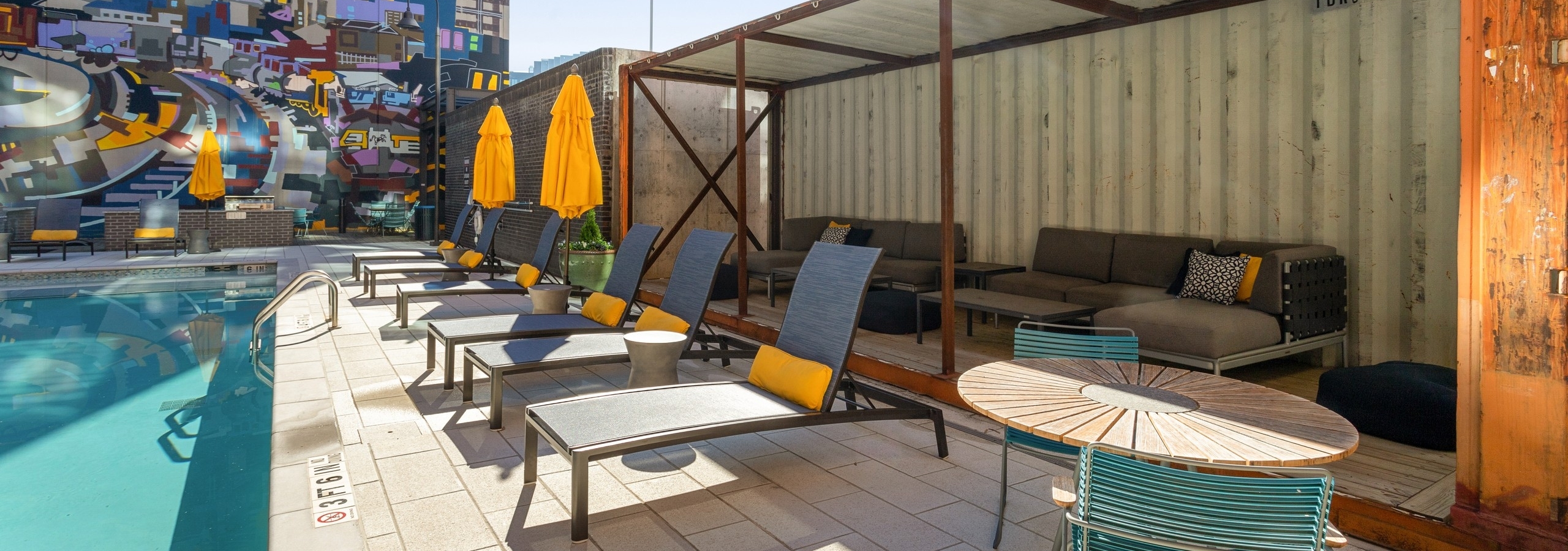 Daytime view of rustic cabana by salt water pool at AMLI Westside apartments with cushioned lounge seating and colorful mural