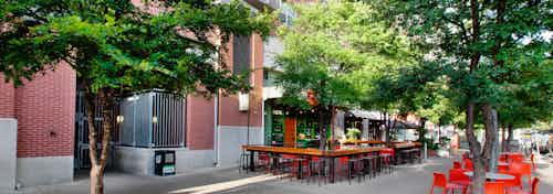 Exterior of retail shop on the first level of AMLI Downtown with orange outdoor barstools and tables with surrounding trees