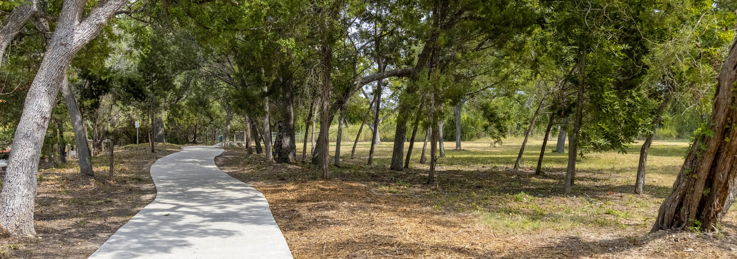 AMLI Covered Bridge daytime view of trail with concrete walkway with mulch and grass and lush green trees