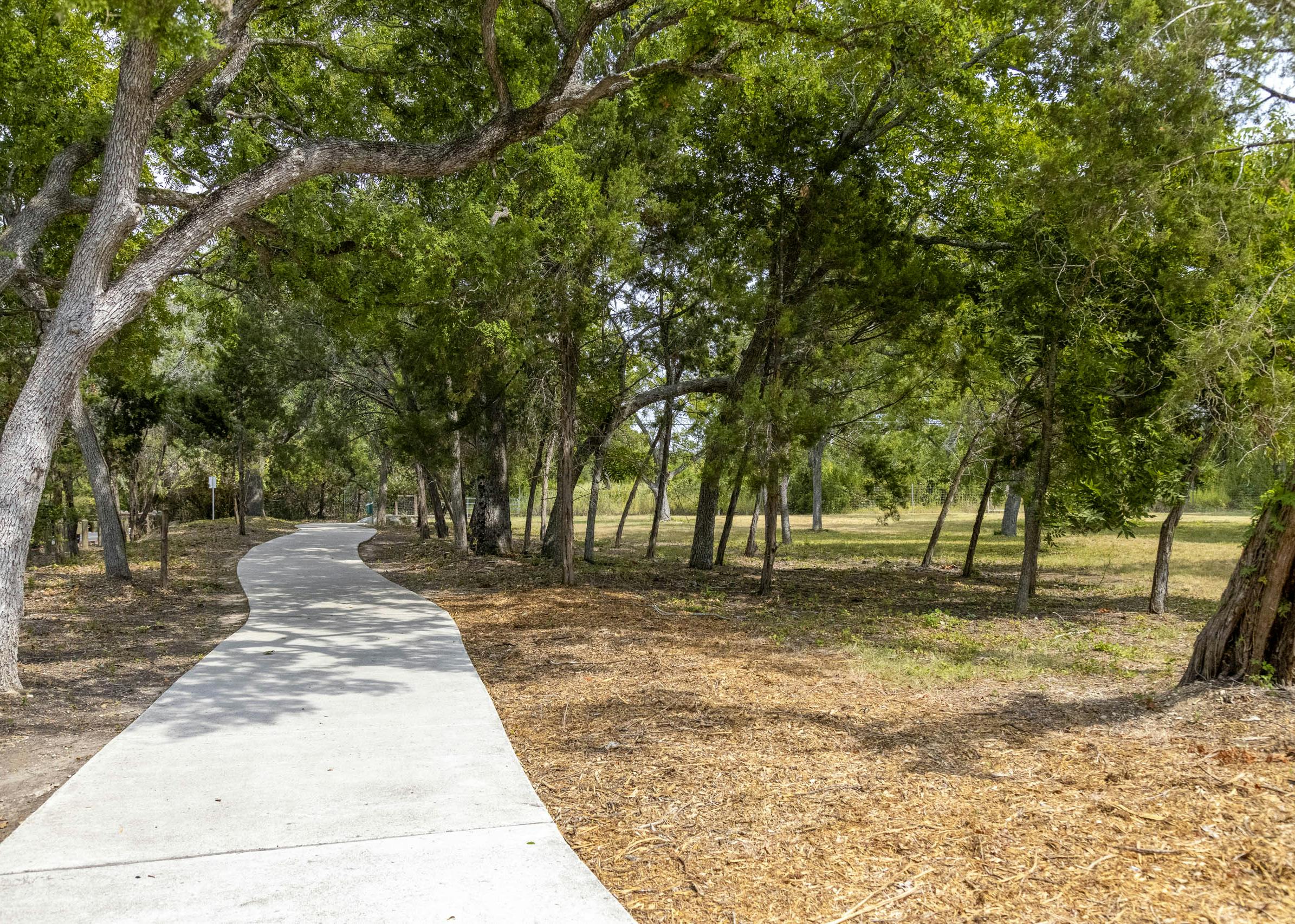 AMLI Covered Bridge daytime view of trail with concrete walkway with mulch and grass and lush green trees