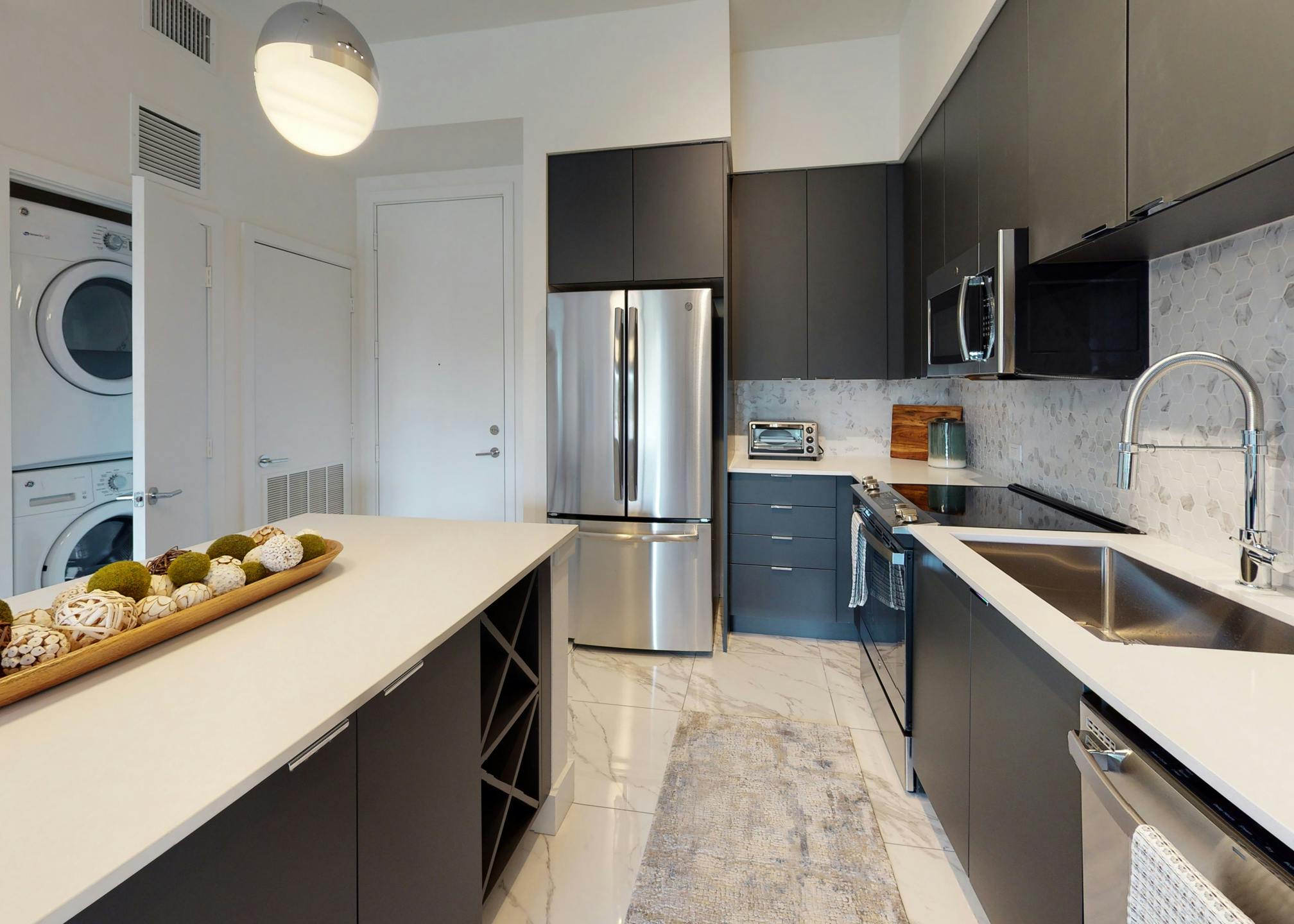 Kitchen at AMLI Park West apartments with dark cabinetry and white quartz counters and marble floors and stacked washer/dryer