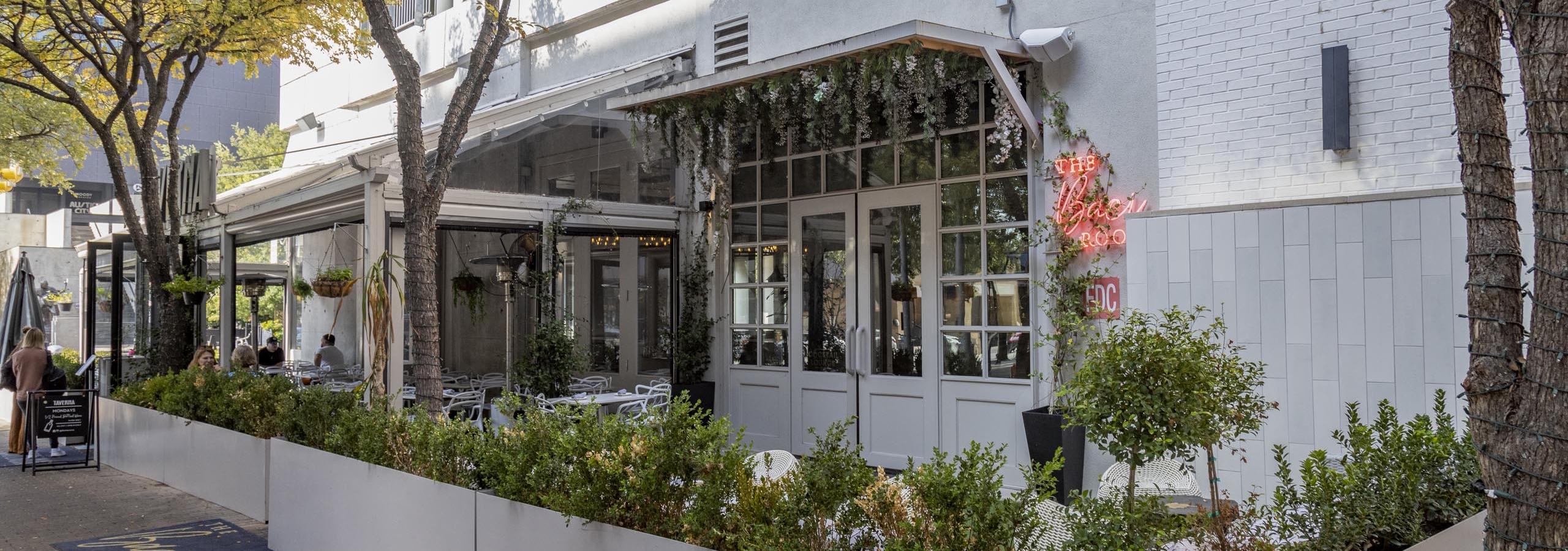 The Bacci Room exterior daytime photo featuring white glass doors with flowers handing from above and outdoor seating