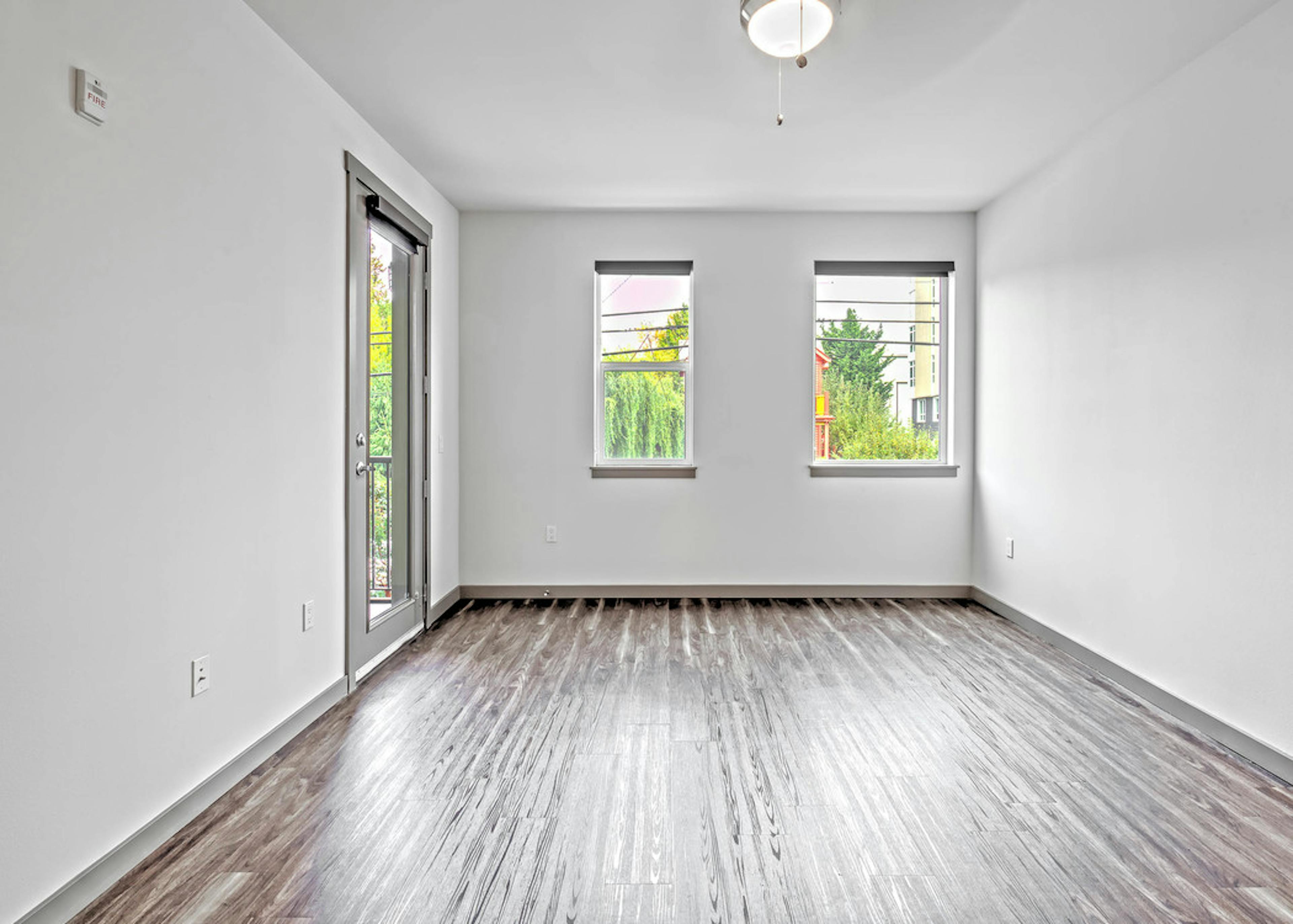 Interior view of AMLI Mark24 living room with laminate floor large windows white walls and door to patio  