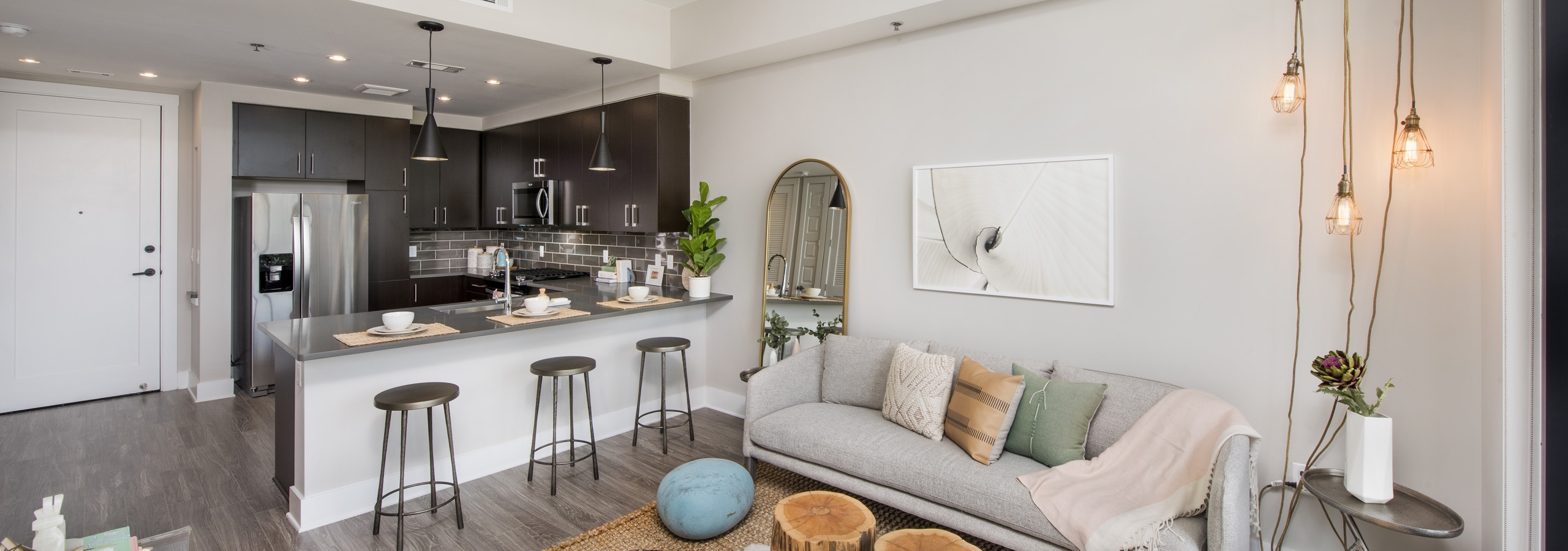Interior of AMLI Lenox apartment with light sofa and hanging lights and three bar stools at an island overlooking the kitchen