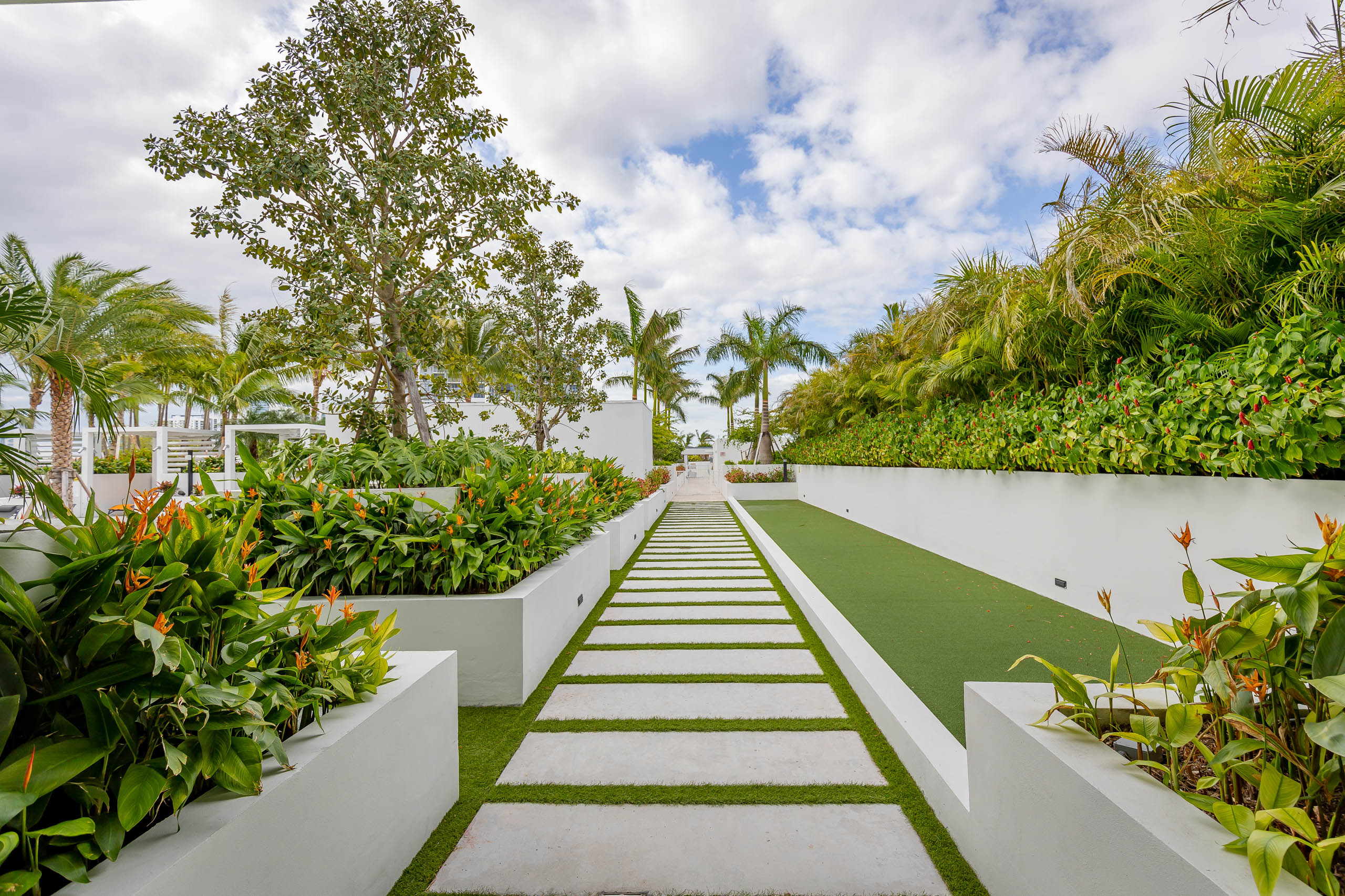 AMLI Midtown Miami apartments courtyard with a faux grass pathway and stepping pavers with lush landscape and planter boxes 