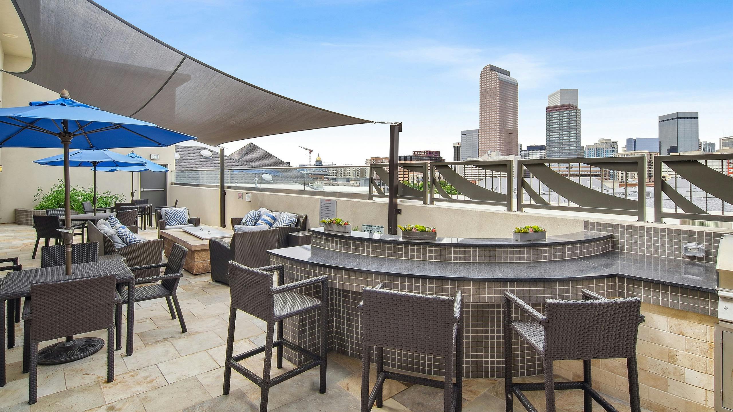 Exterior view of a rooftop lounge at AMLI Park Avenue with a bar seating area with chairs and tables with blue umbrellas