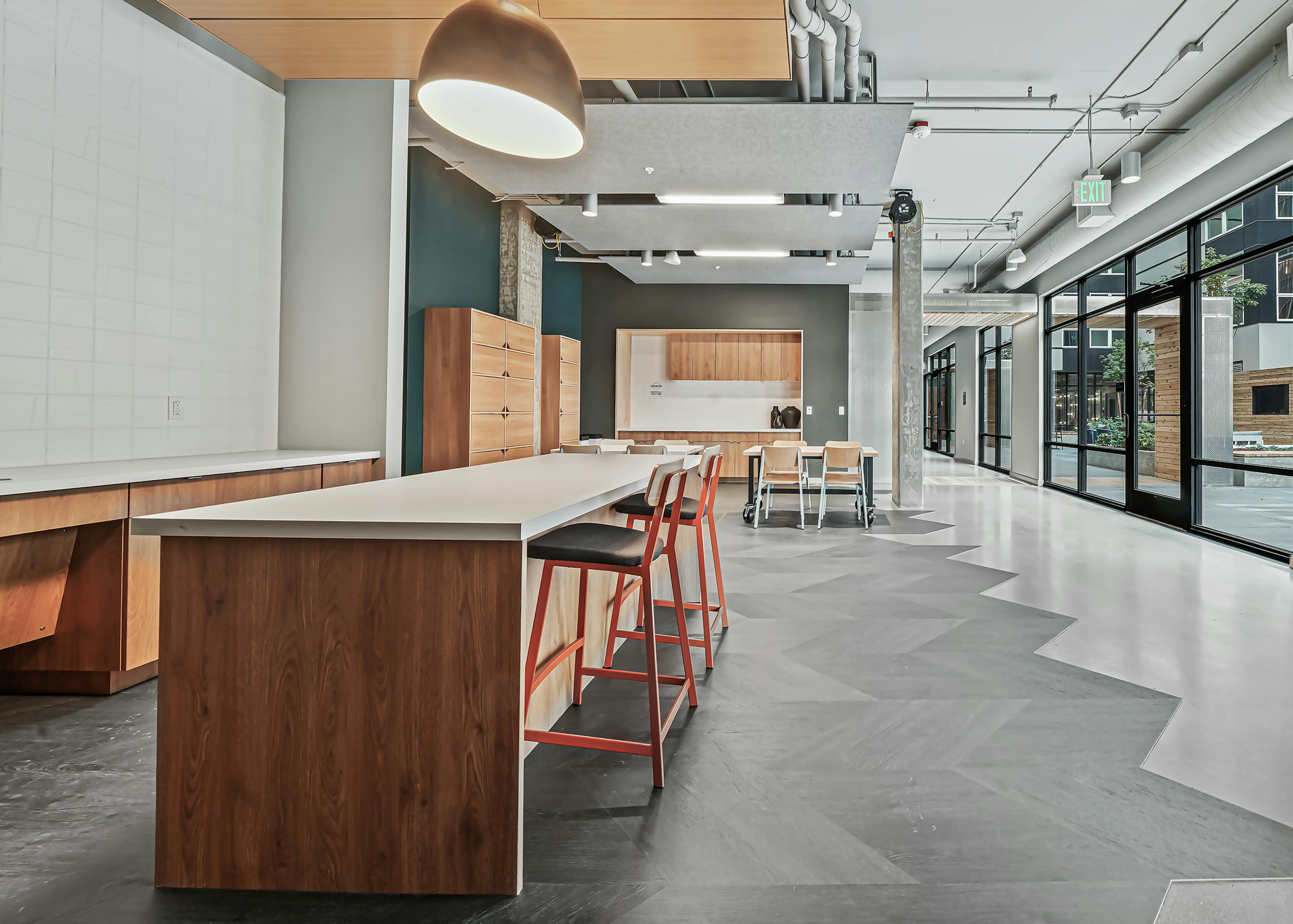 Interior view of AMLI Spring District maker space with long island with chairs and other tables and wood storage cabinets