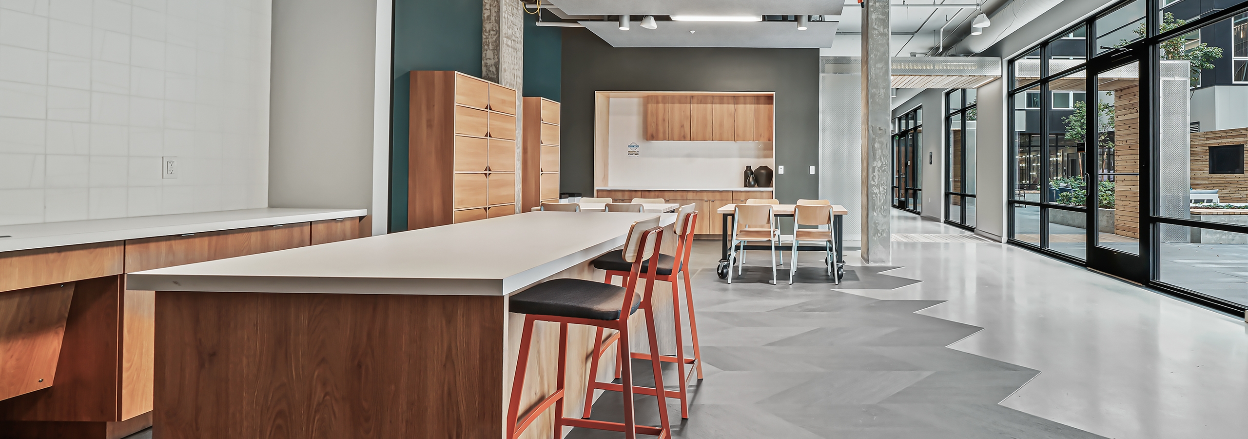 Interior view of AMLI Spring District maker space with long island with chairs and other tables and wood storage cabinets