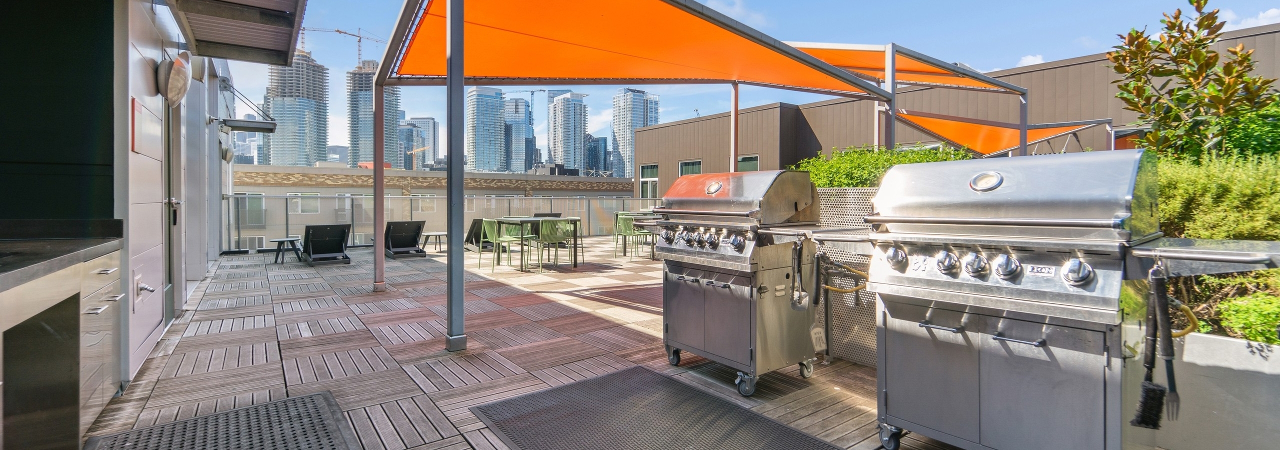 Rooftop deck at AMLI South Lake Union with two stainless steel grills as well as tables and chairs with orange canopies