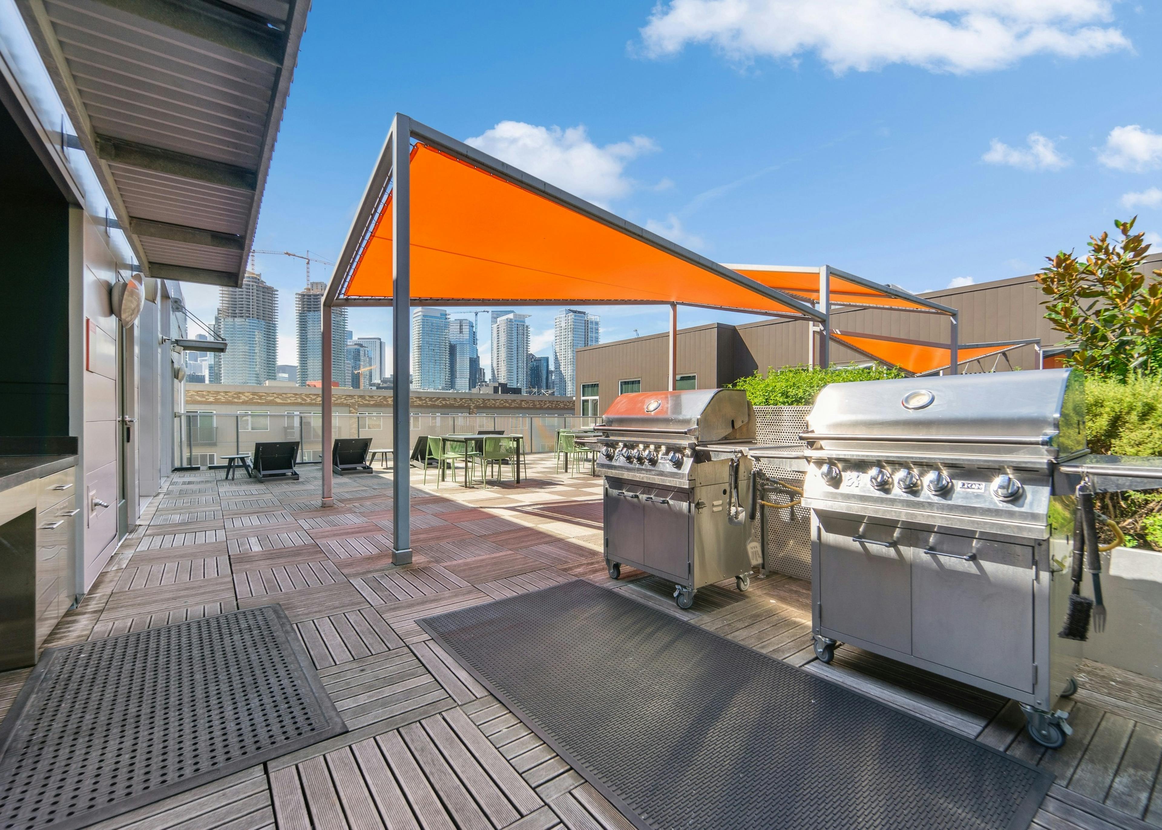 Rooftop deck at AMLI South Lake Union with two stainless steel grills as well as tables and chairs with orange canopies