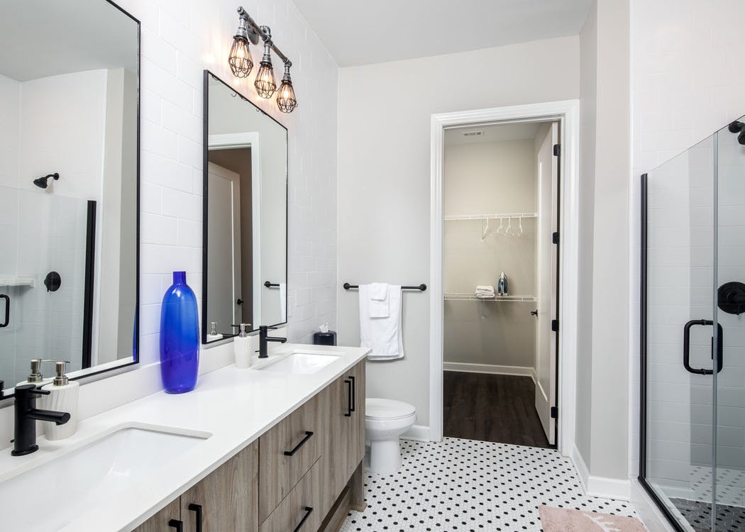 AMLI Westside bathroom with a double sink vanity and black and white tiled floors with a toilet and peek into walk in closet