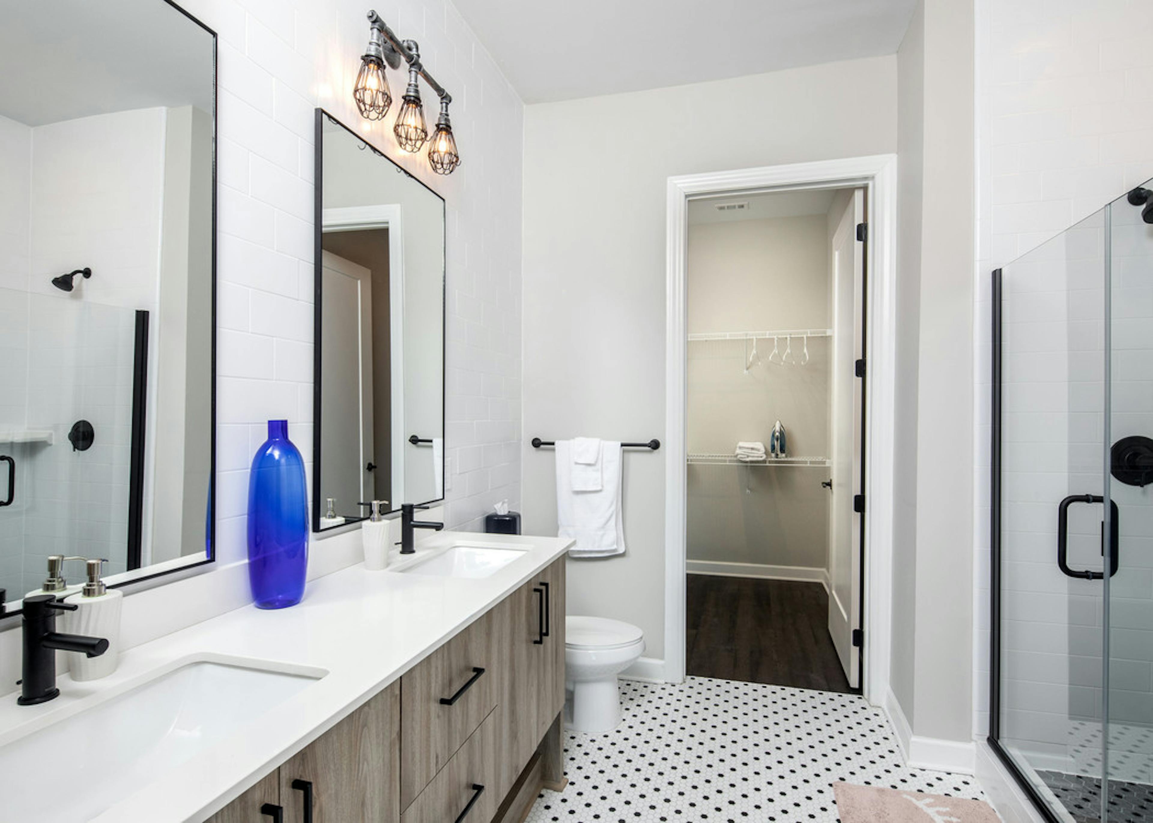 AMLI Westside bathroom with a double sink vanity and black and white tiled floors with a toilet and peek into walk in closet