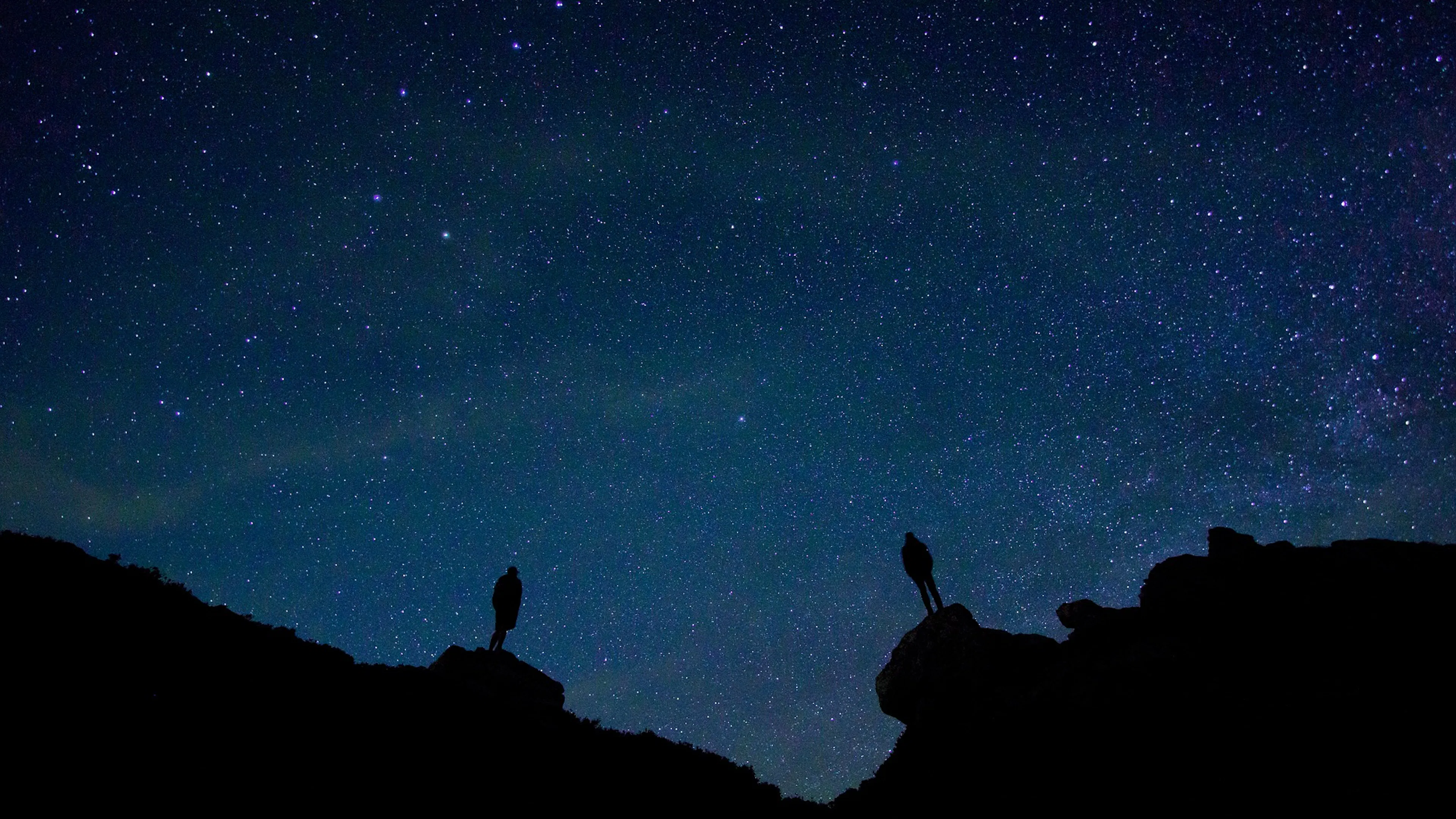 The silhouettes of two people stargazing and looking up at the Milky Way