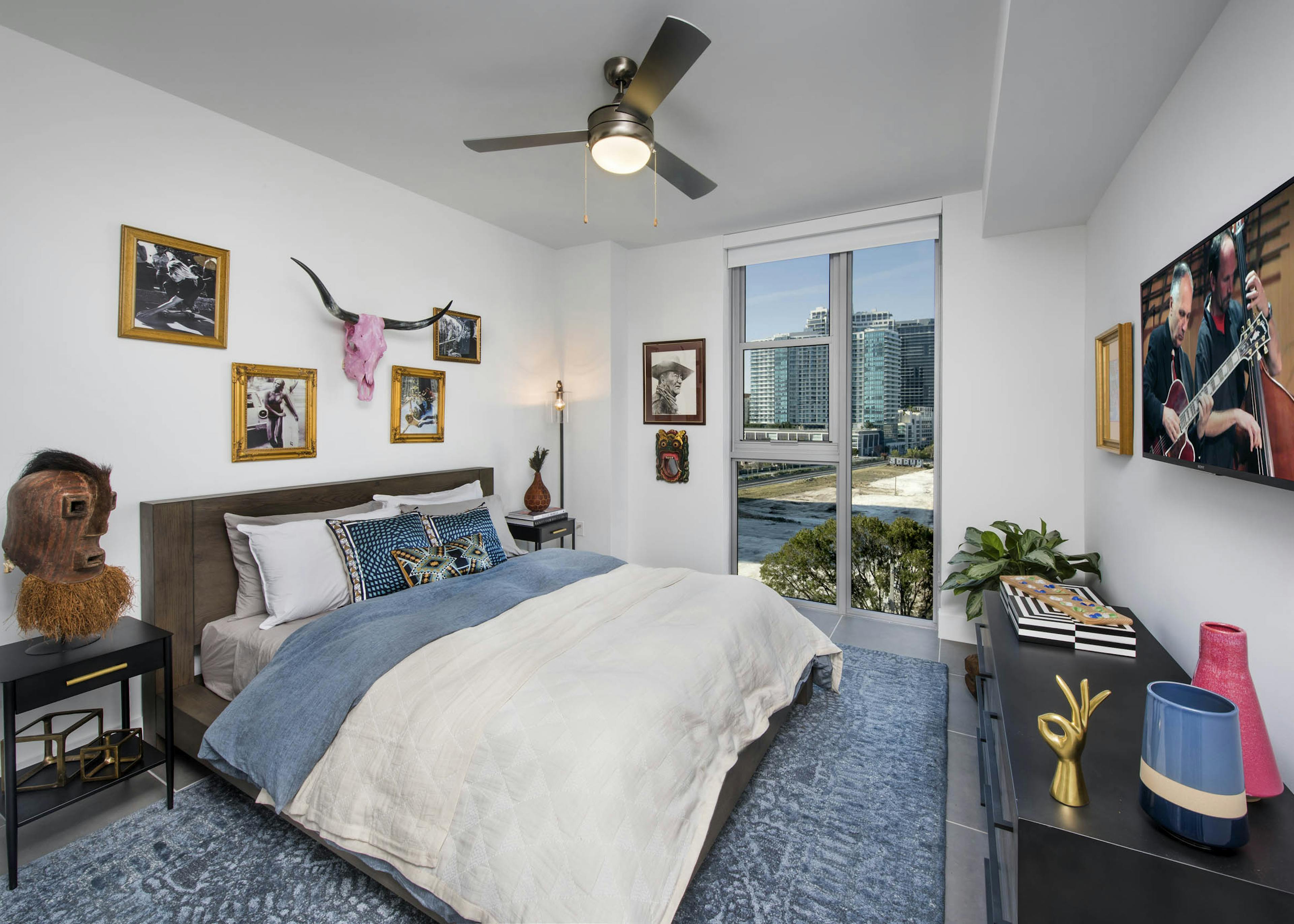Bedroom with a city view and pink skull with horns over bed with white and blue blankets and blue carpet at AMLI Midtown 29