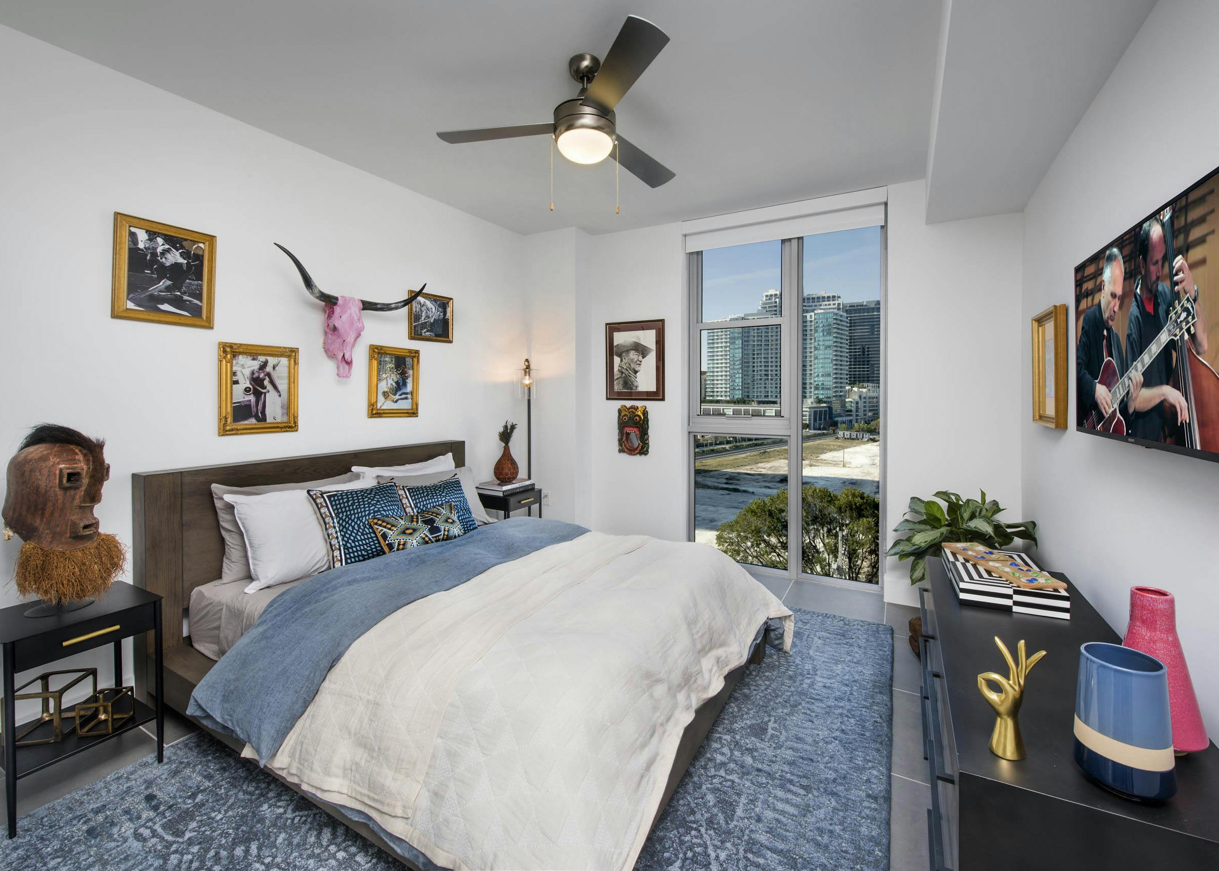 Bedroom with a city view and pink skull with horns over bed with white and blue blankets and blue carpet at AMLI Midtown 29