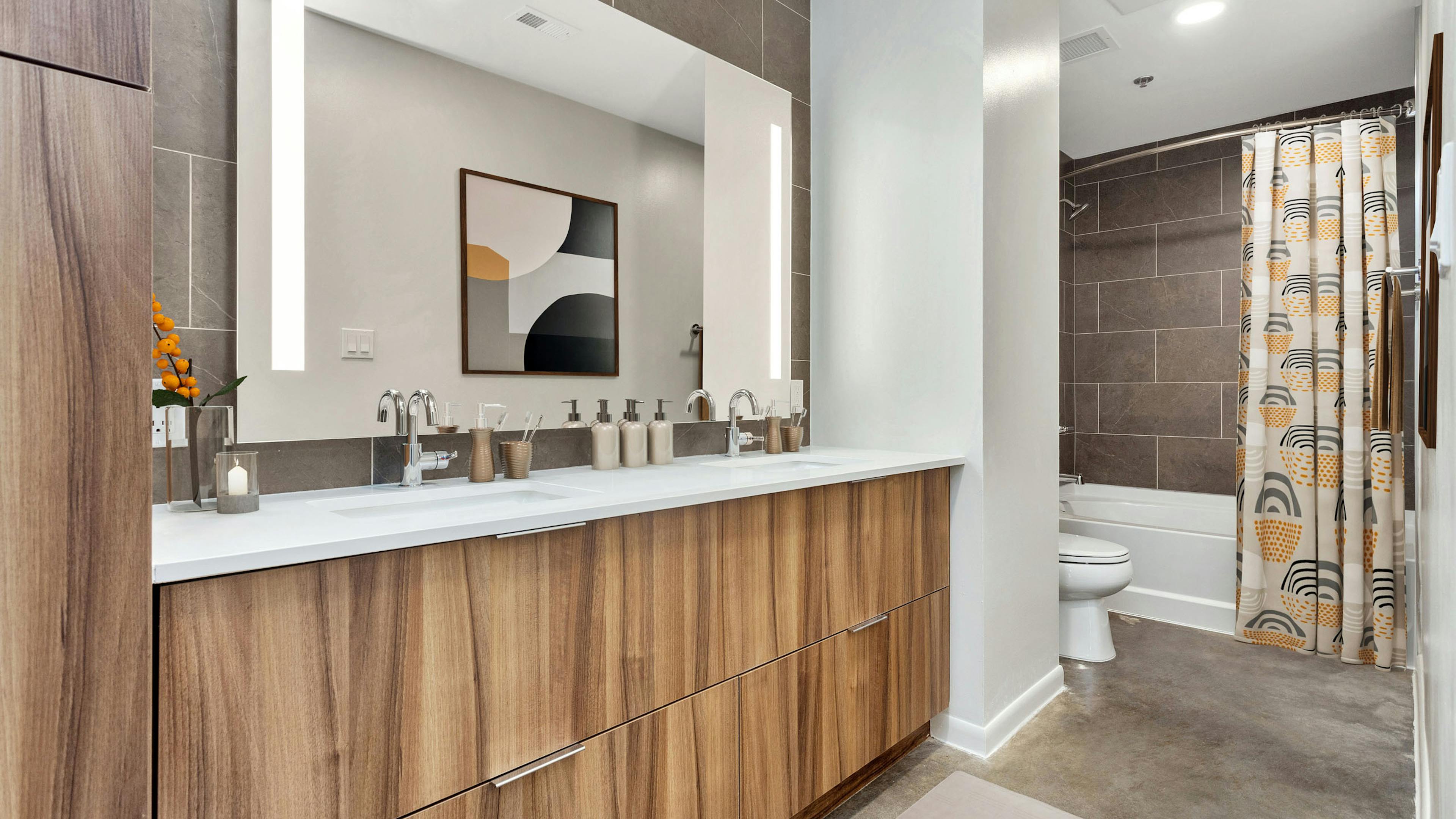 AMLI on 2nd bathroom with wood cabinetry and white countertop below large mirror and white bathtub with brown tile surround