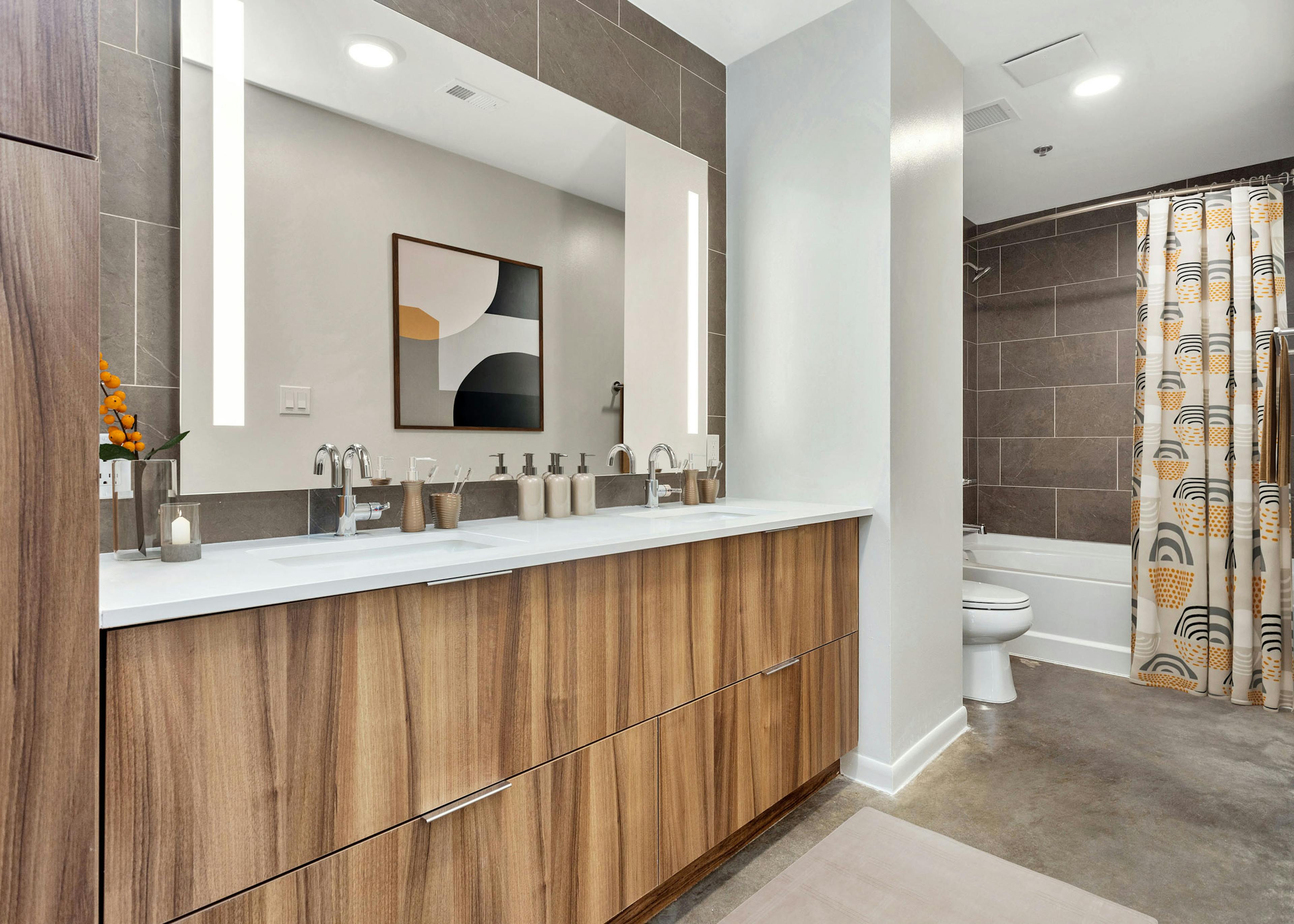 AMLI on 2nd bathroom with wood cabinetry and white countertop below large mirror and white bathtub with brown tile surround