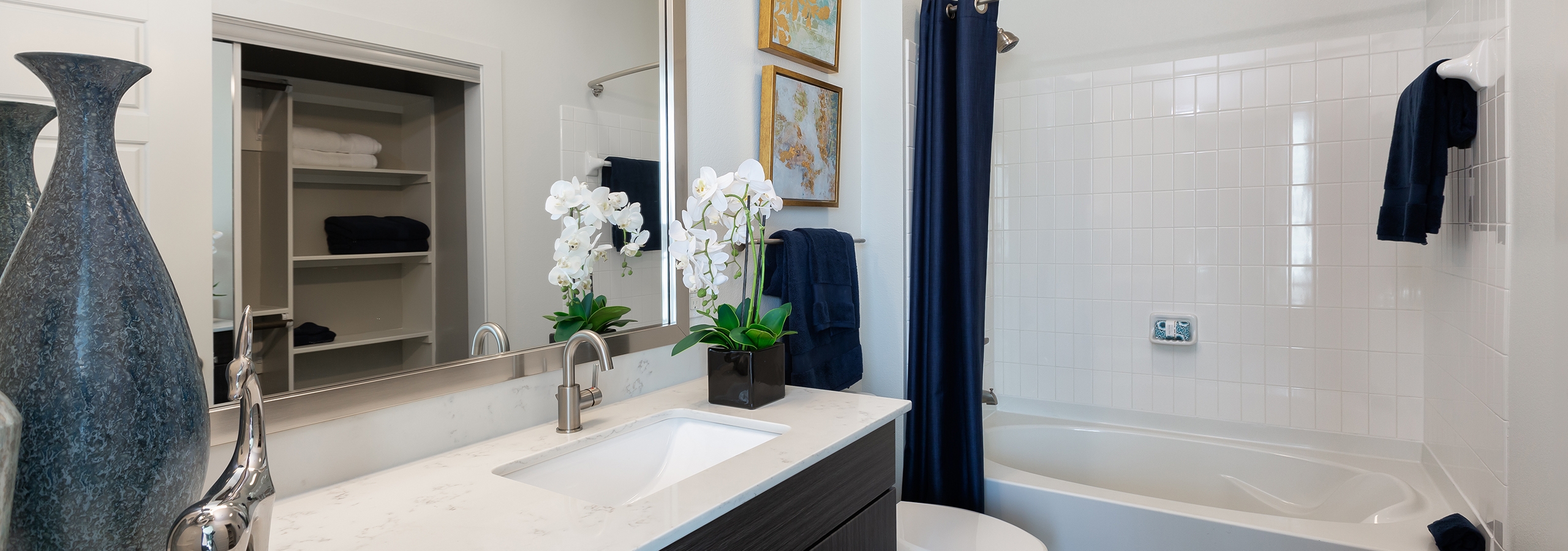 Apartment bathroom at AMLI South Shore with a large blue vase resting on quartz vanity sink countertop with white shower tub