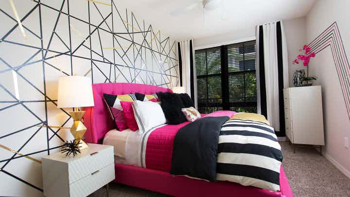 AMLI Dadeland master bedroom with geometric accent wall, modern table lamp, magenta and black bedding and a window view