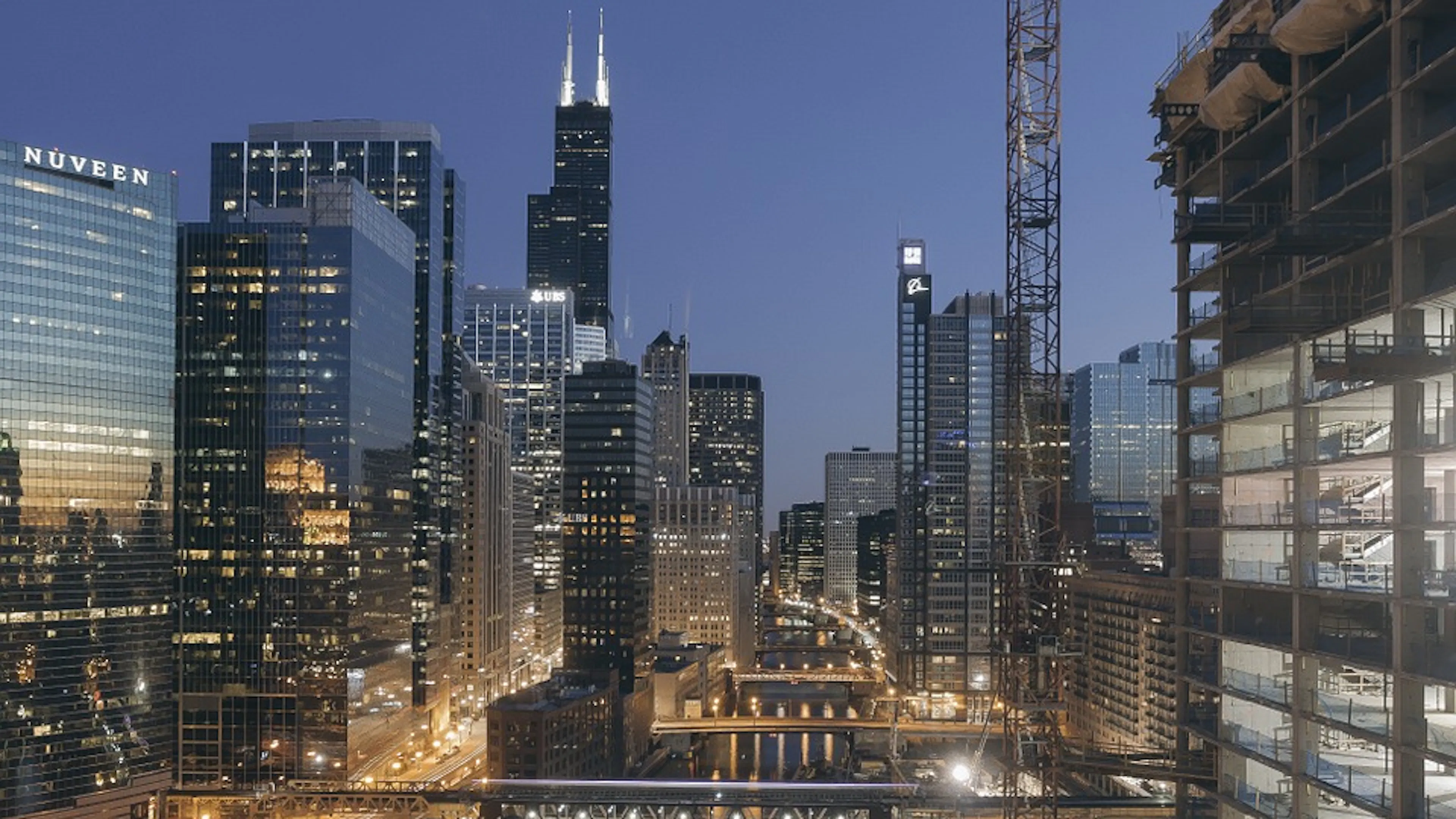The Chicago River winding through the city at dusk with a few lights reflecting in the still water
