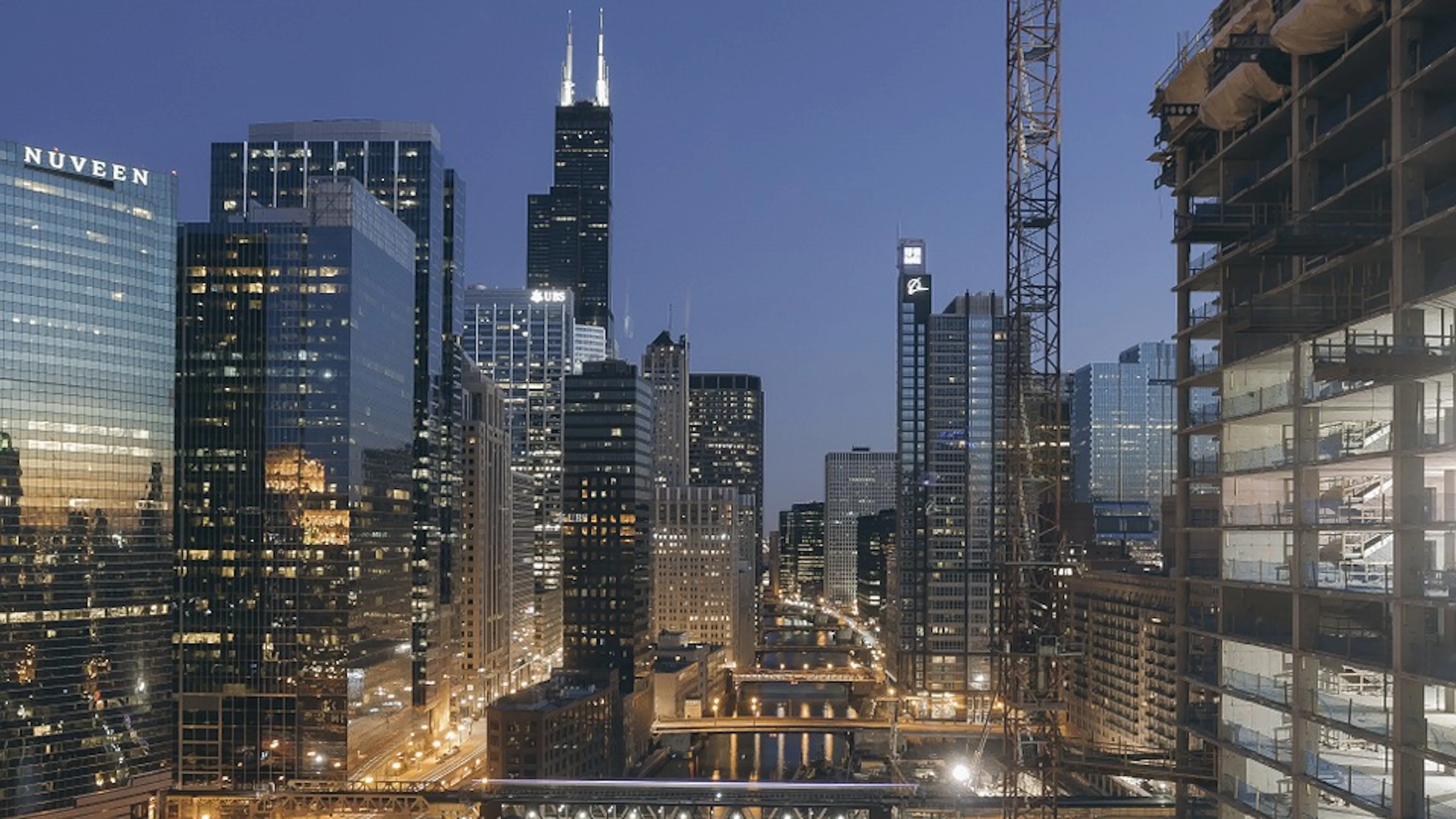 The Chicago River winding through the city at dusk with a few lights reflecting in the still water