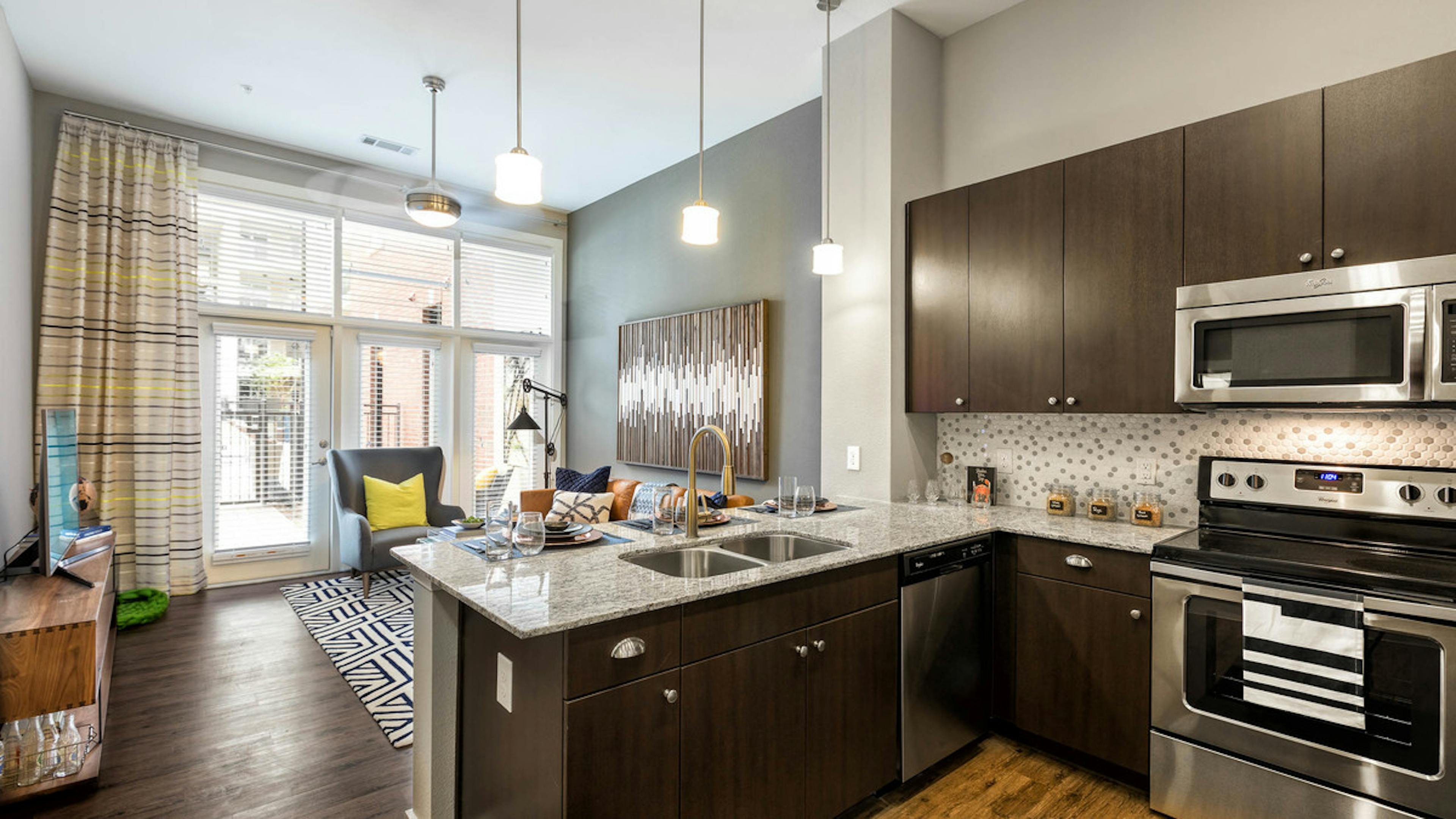 Interior view of AMLI Frisco Crossing apartment kitchen with stainless steel appliances and living room with large windows