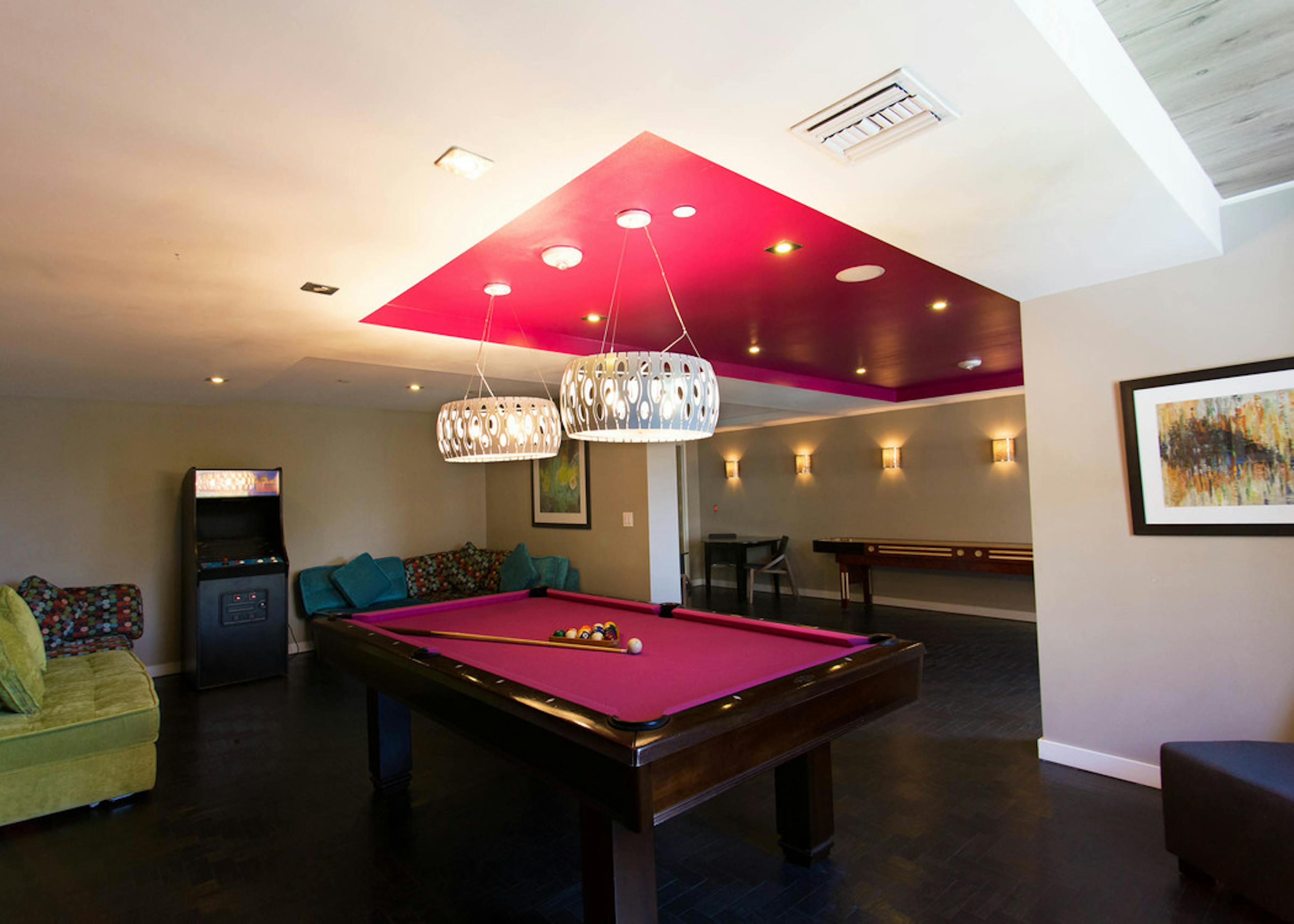 Interior game lounge at AMLI Dadeland with vibrant colored billiards table, arcade game and plush seating 