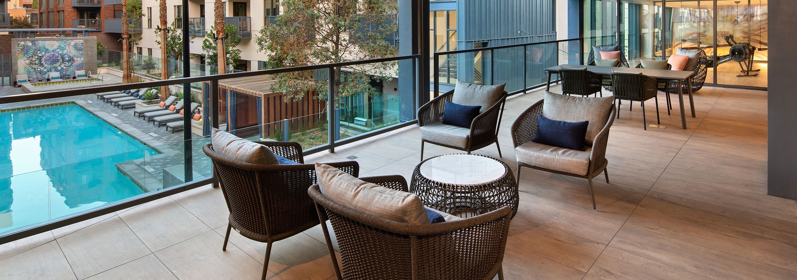 Daytime view of covered terrace with lounge seating that overlooks the pool and palm trees at AMLI Old Pasadena apartments
