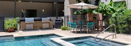 Exterior view of daytime AMLI 300 poolside gas-grills and dining area with teal chairs and an umbrella-shaded table