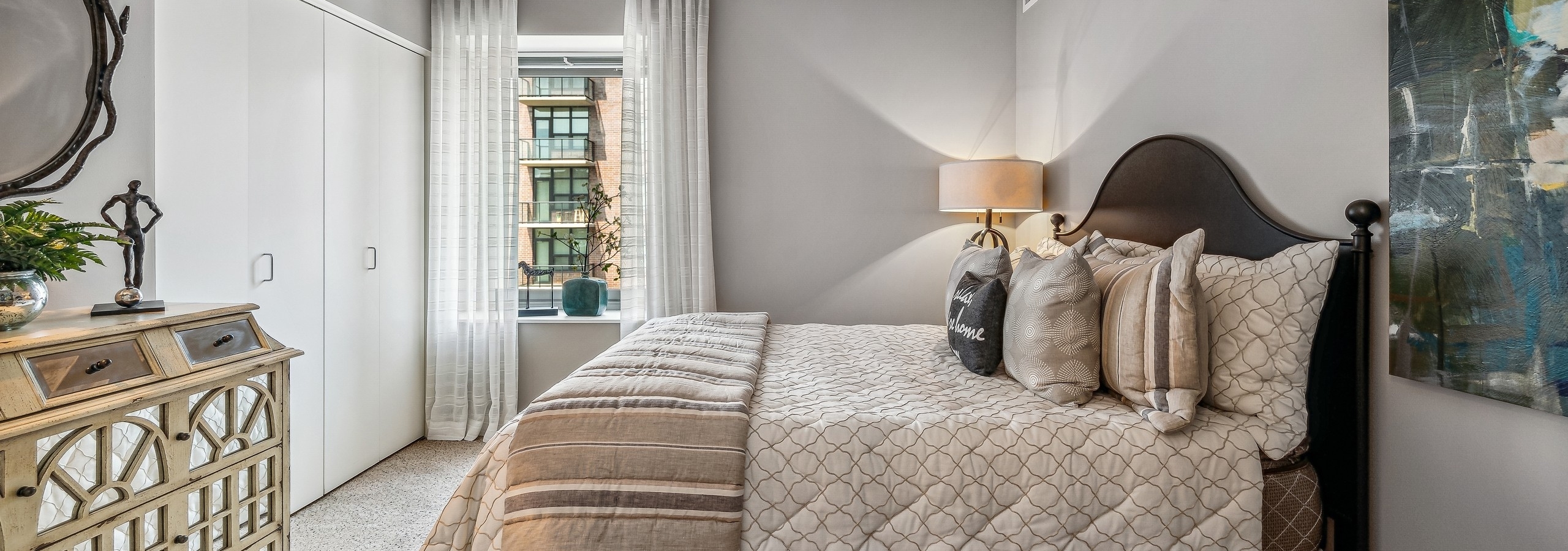 Bedroom with dark wood bed and beige and brown bedding and window with white curtains and gray walls at AMLI 900 apartments