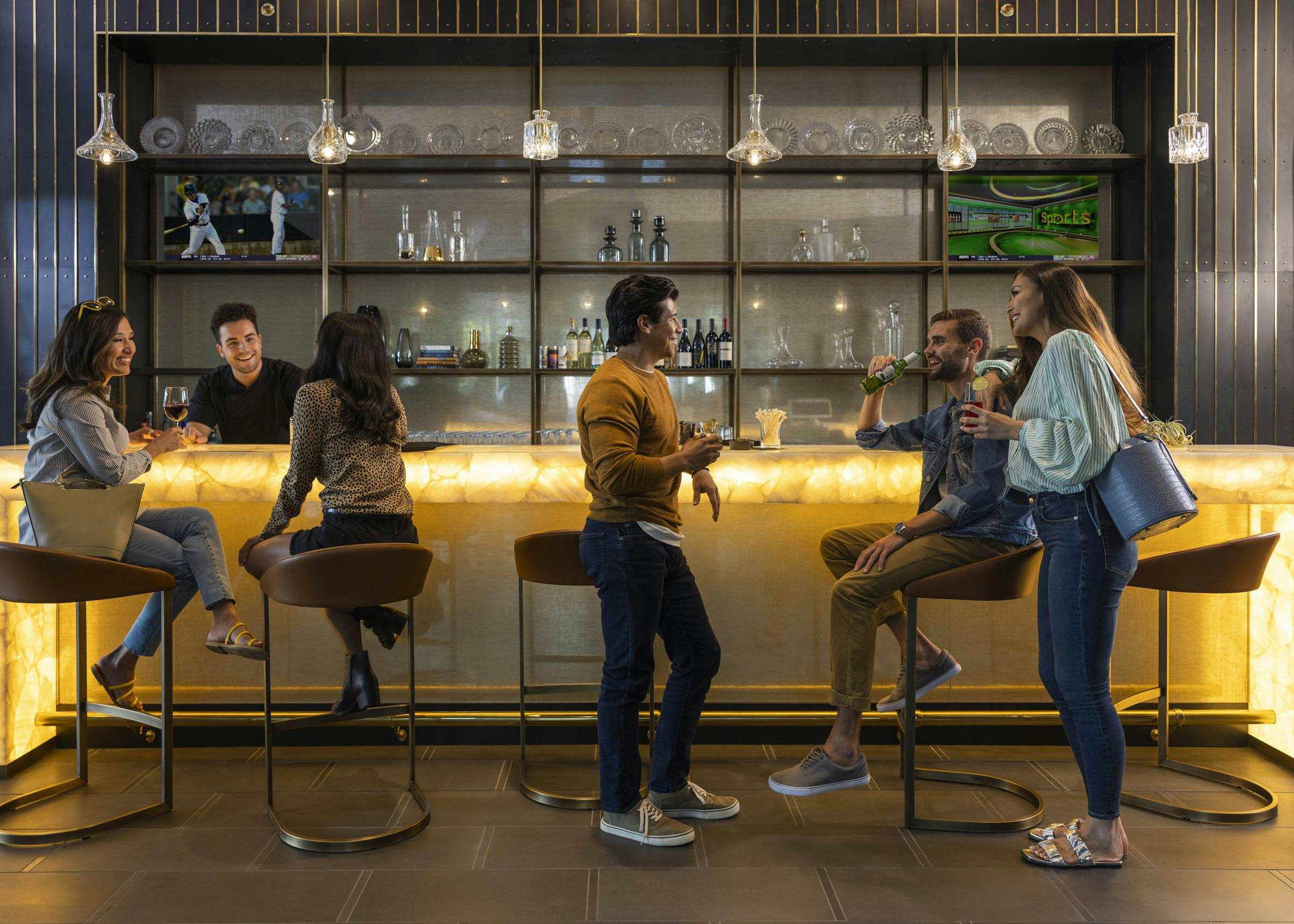 A group of AMLI Fountain Place residents enjoying community bar area with an illuminated bar and decorative hanging lights