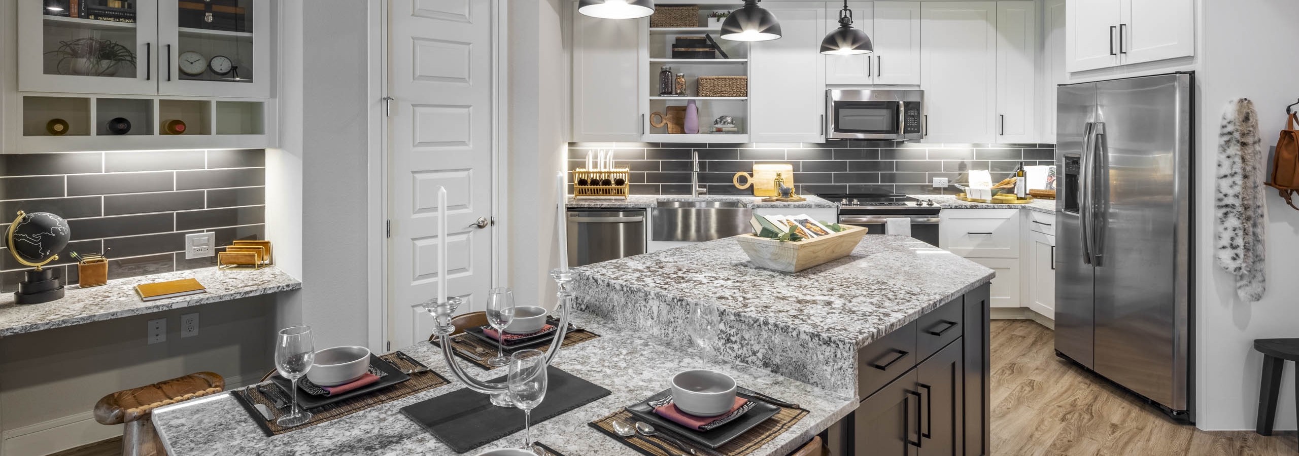 AMLI Lakeline apartment kitchen featuring gray granite countertops and white cabinets against a black tile backsplash