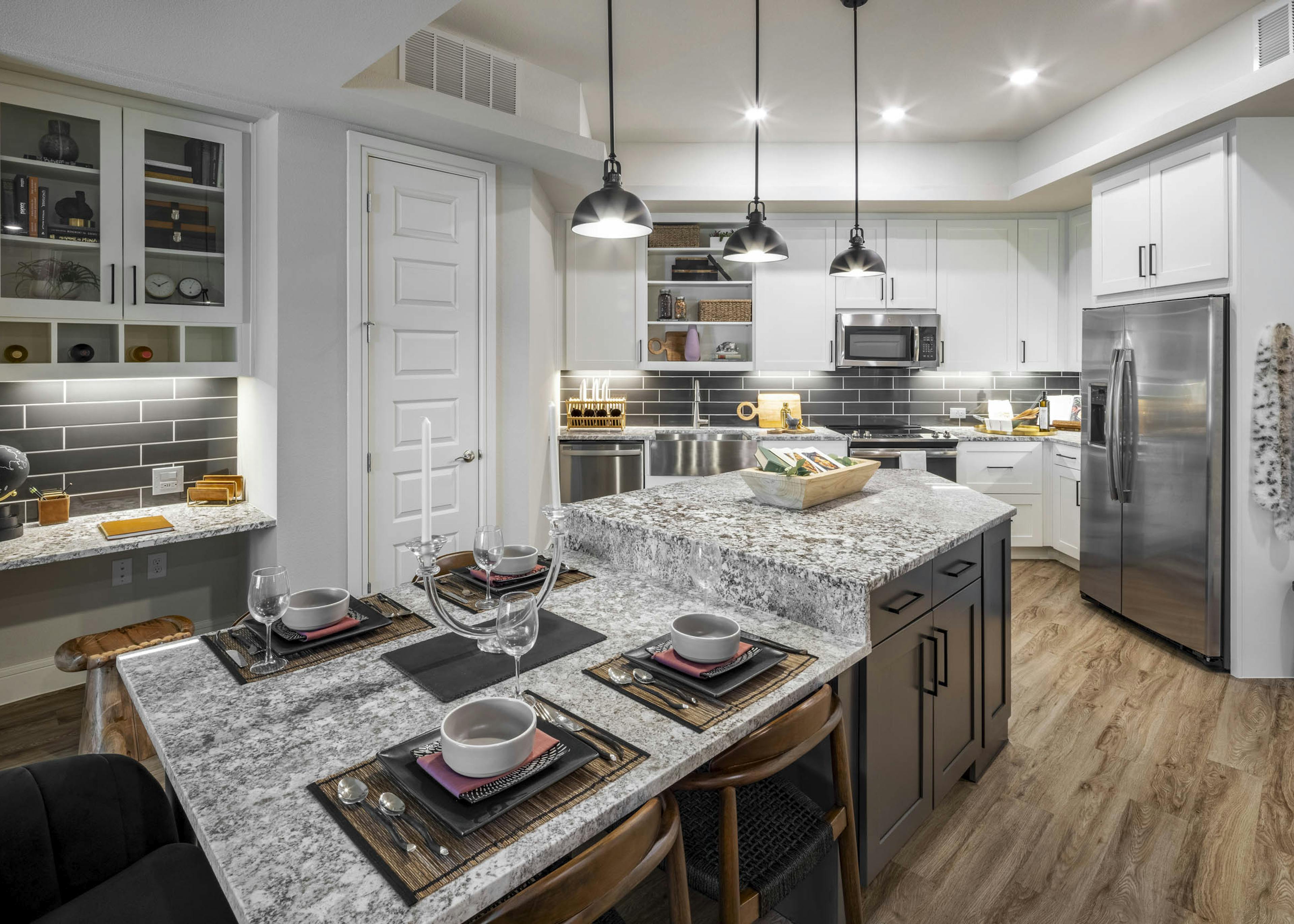 AMLI Lakeline apartment kitchen featuring gray granite countertops and white cabinets against a black tile backsplash