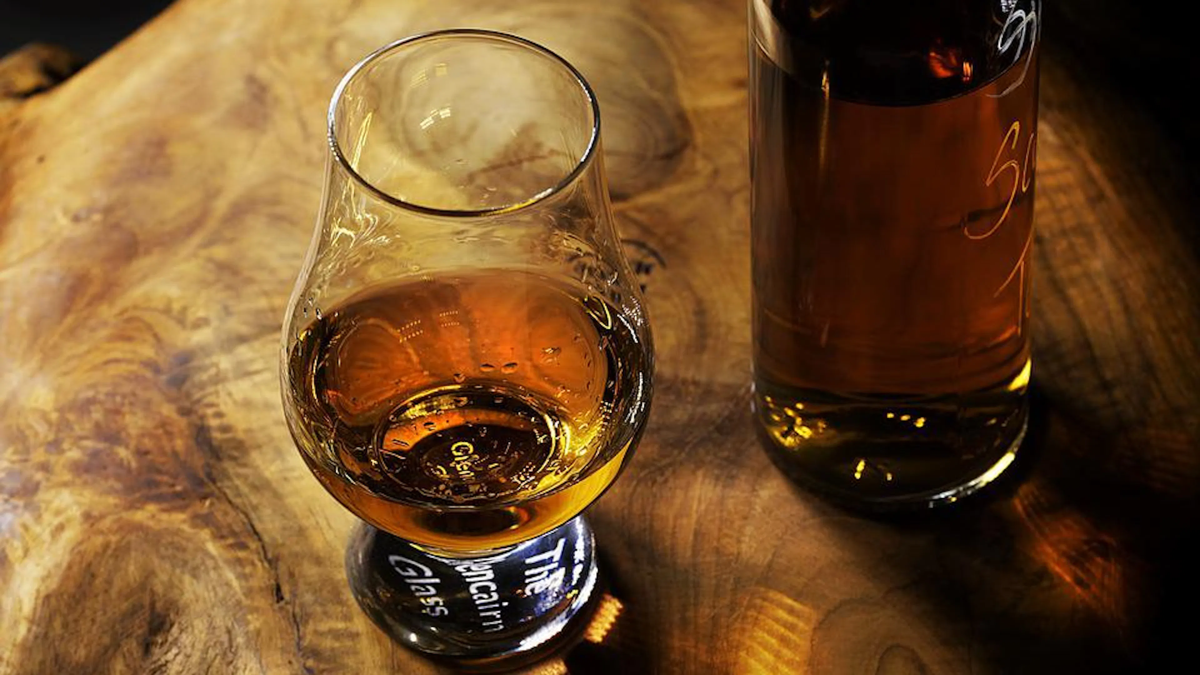 Two glasses filled with whiskey on a wooden table under dim light