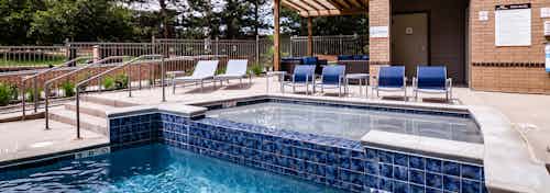 A hot tub at AMLI Dry Creek apartments with blue tile and blue lounge chairs with lush green trees and grass in background