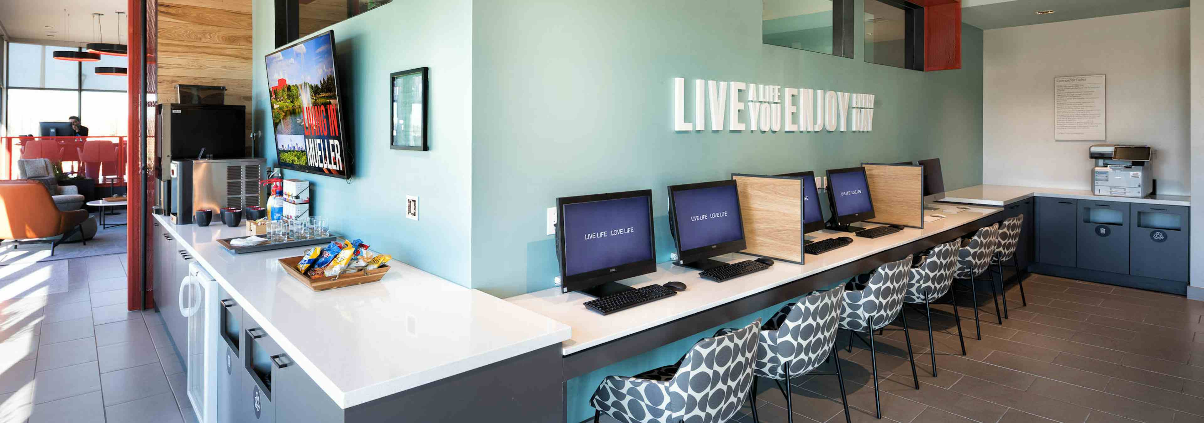 Tech lounge at AMLI on Aldrich with desktop computers at a long white desk against a light teal wall with patterned chairs