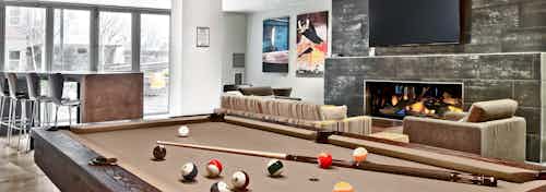 AMLI Mark24 clubroom with billiards table in foreground with cue and balls and cozy seating and big screen TV by fireplace