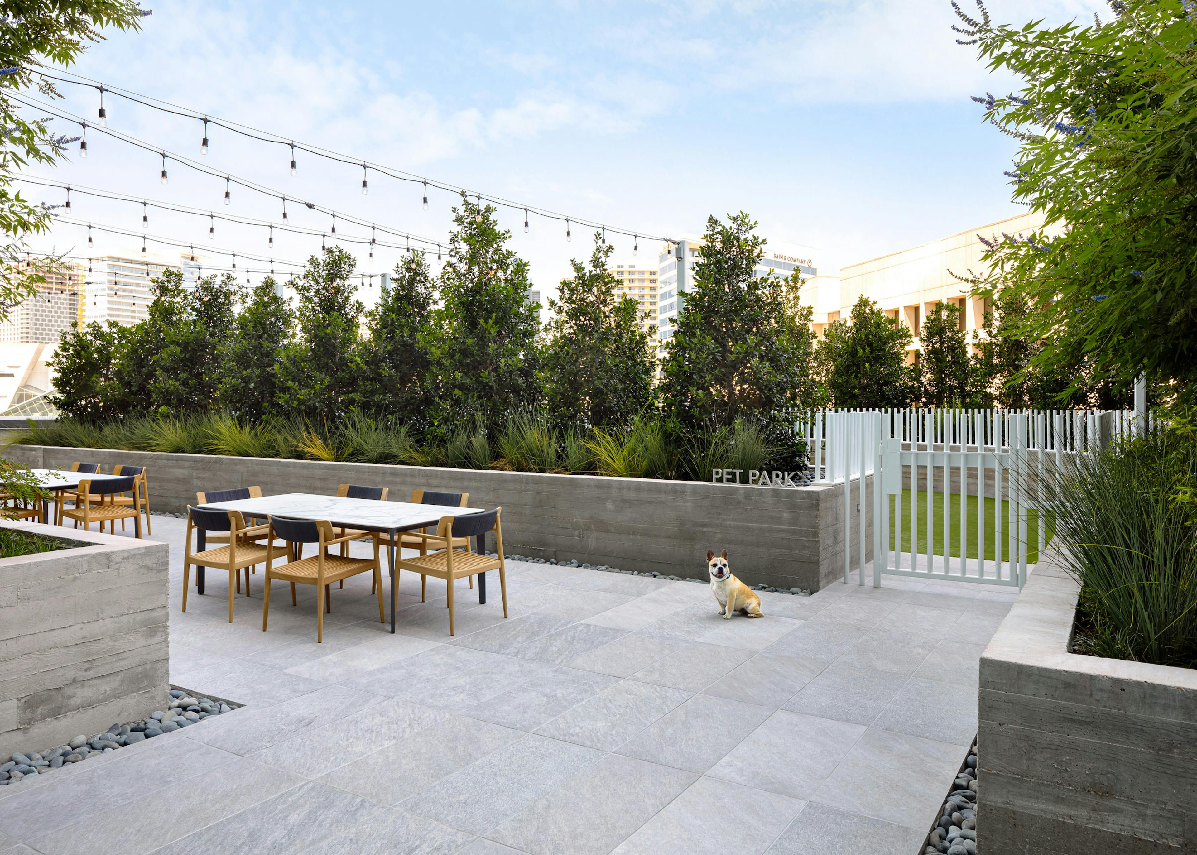 AMLI Fountain Place pet park entrance with white fence and adjacent landscaped outdoor seating with lights hanging above
