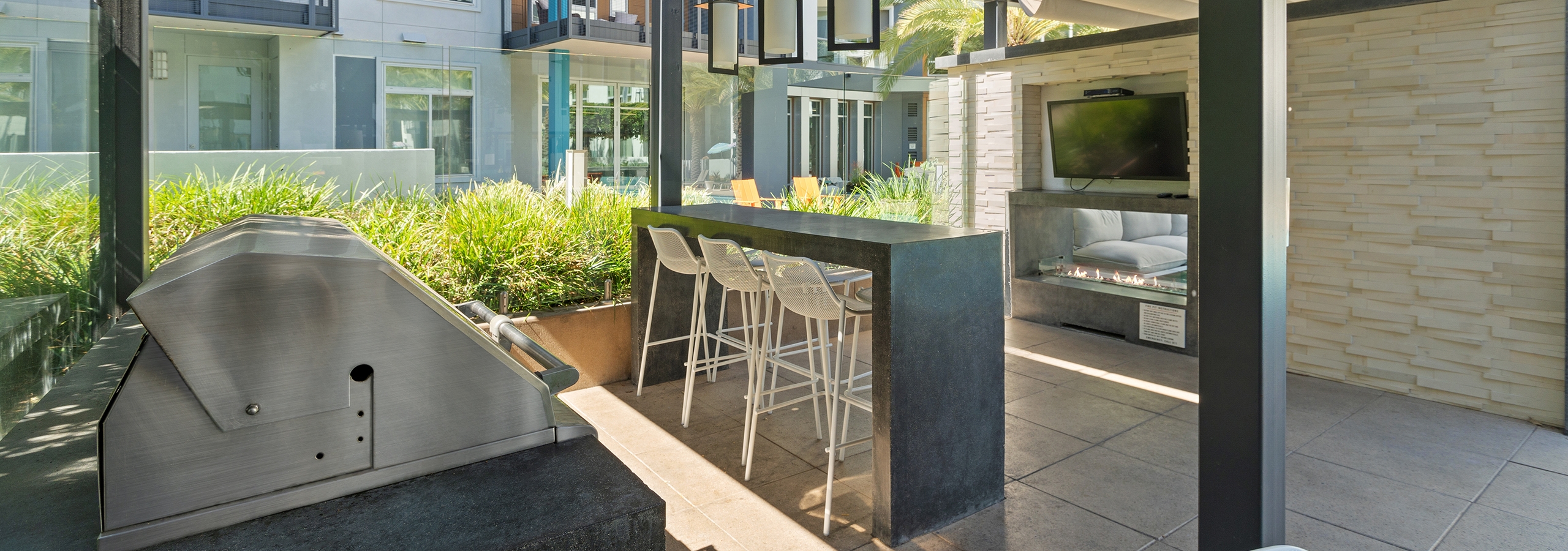 Daytime view of grill area at AMLI Uptown Orange with hightop bar and chairs in front of a big screen TV and lit fireplace