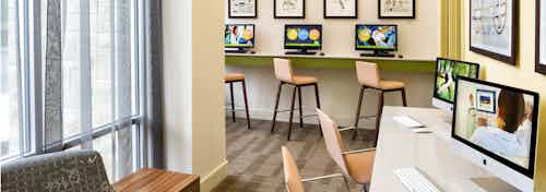 AMLI at Mueller business center with bar stools at a raised counter with desktop computers and light flooring with tall windows